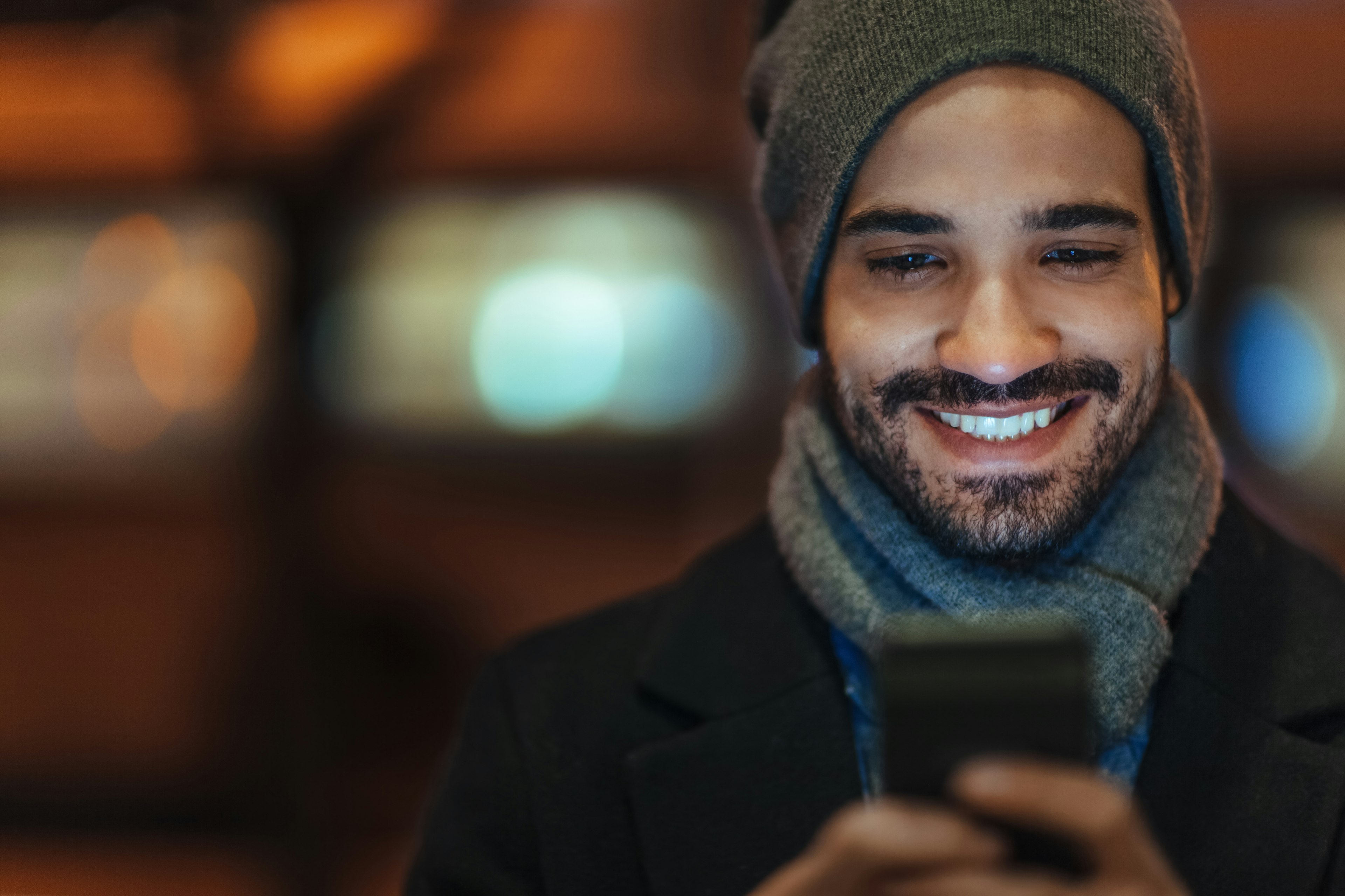 Young man wearing a hat looks at his smartphone on city street at night