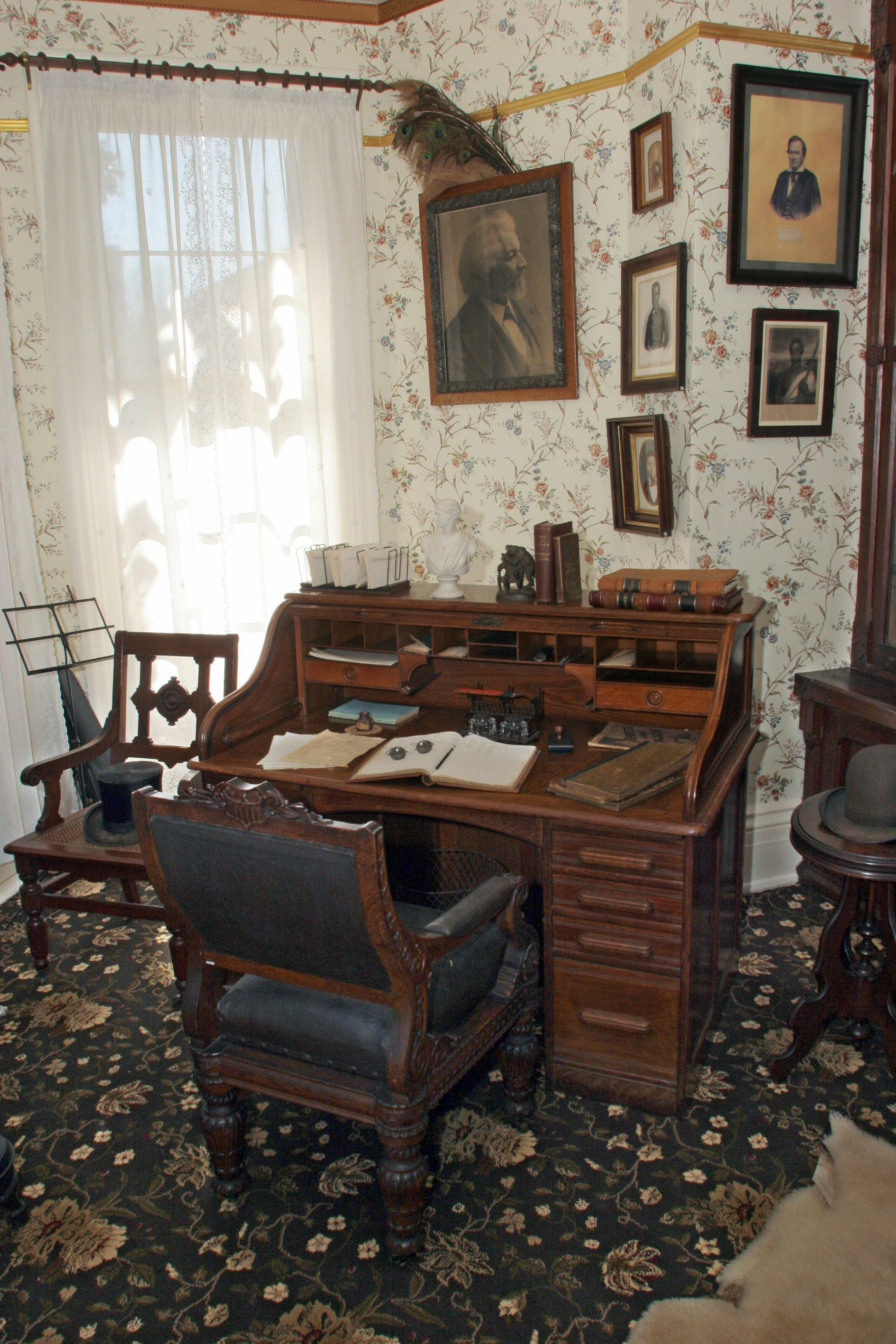 A portrait of a Black man hangs on a wall among other pictures above a desk