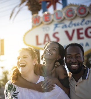 Three friends smile and laugh Las Vegas sign in Las Vegas, Nevada, USA.