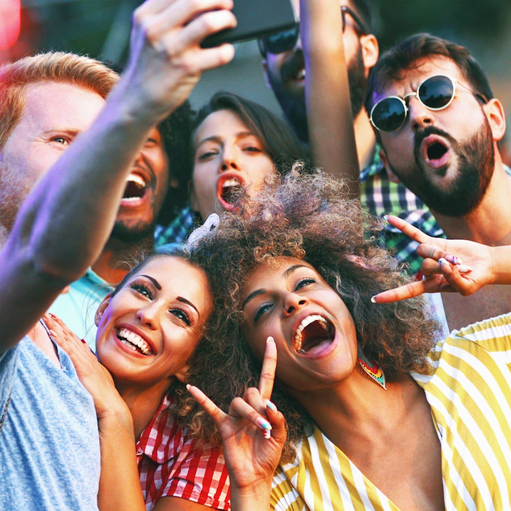 Closeup of group of multi ethnic young adults taking some selfies at an open air concert. The Sun is about to set and they are nicely lit by low and soft sunlight.