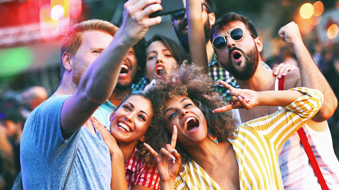 Closeup of group of multi ethnic young adults taking some selfies at an open air concert. The Sun is about to set and they are nicely lit by low and soft sunlight.