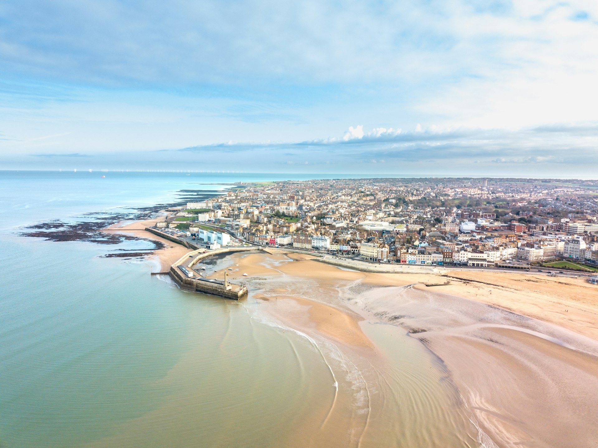 Aerial view of a curve of golden sand in Margate, England, with a concrete harbor arm stretching out into the sea