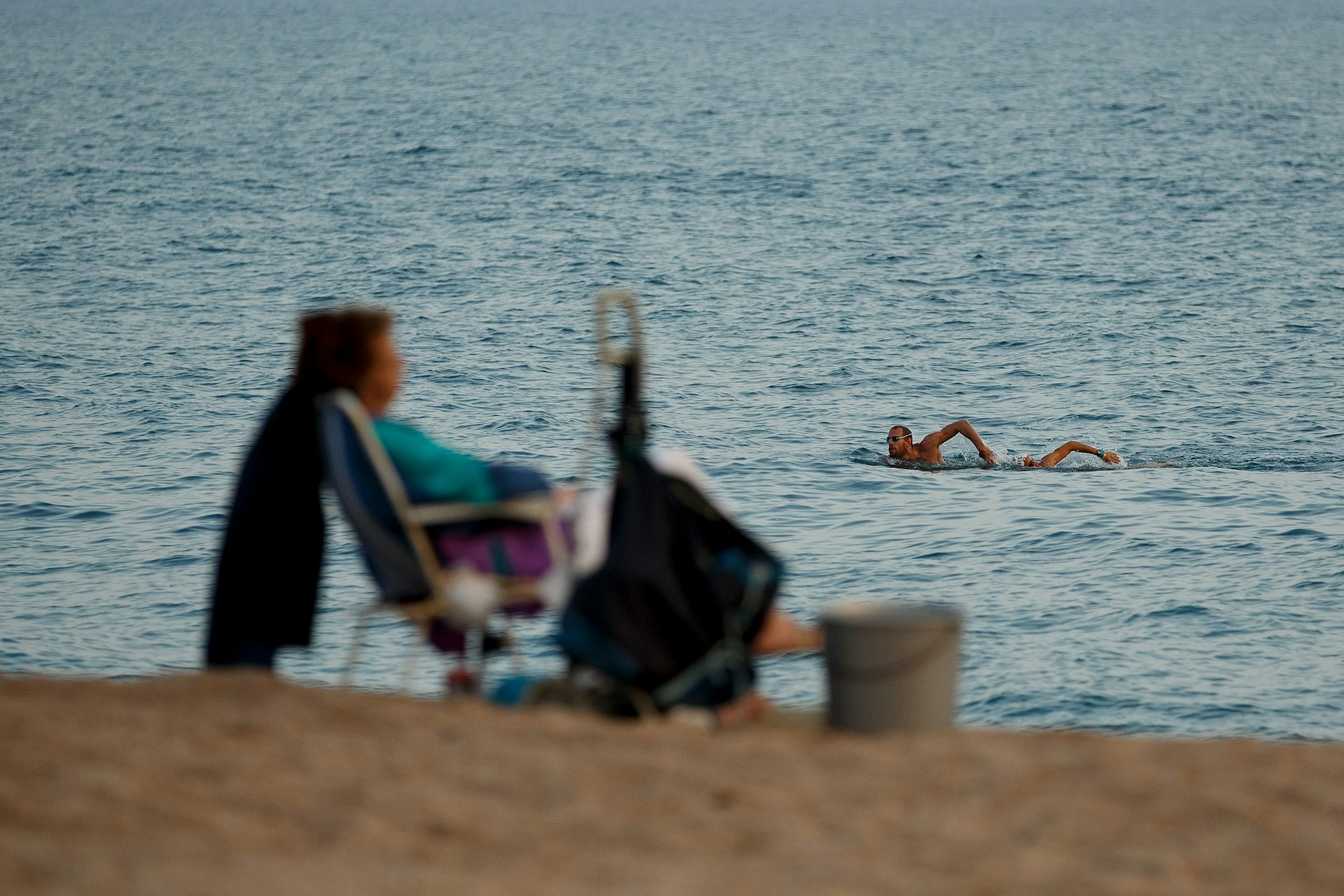 Two Ironman swimmers in the sea near Barcelona swim past the silhouette of an old woman on the beach