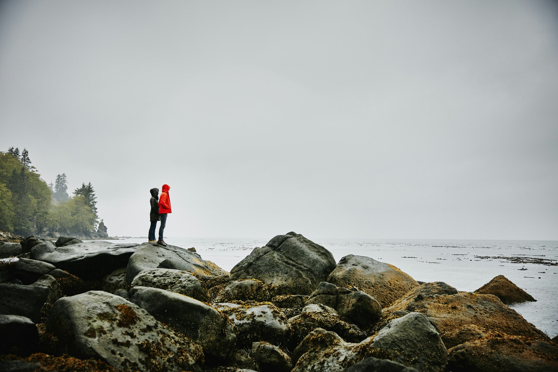 Couple standing on boulders on shoreline of ocean