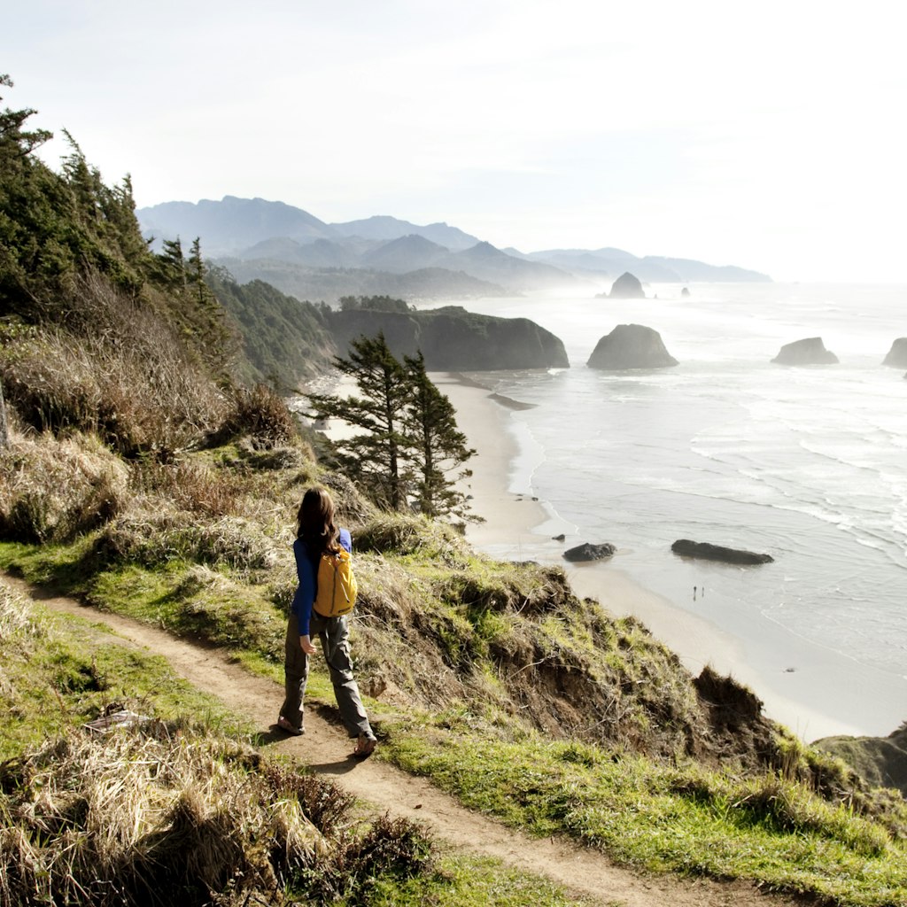 Female hiker walking along a secluded coastline path in Ecola State Park.