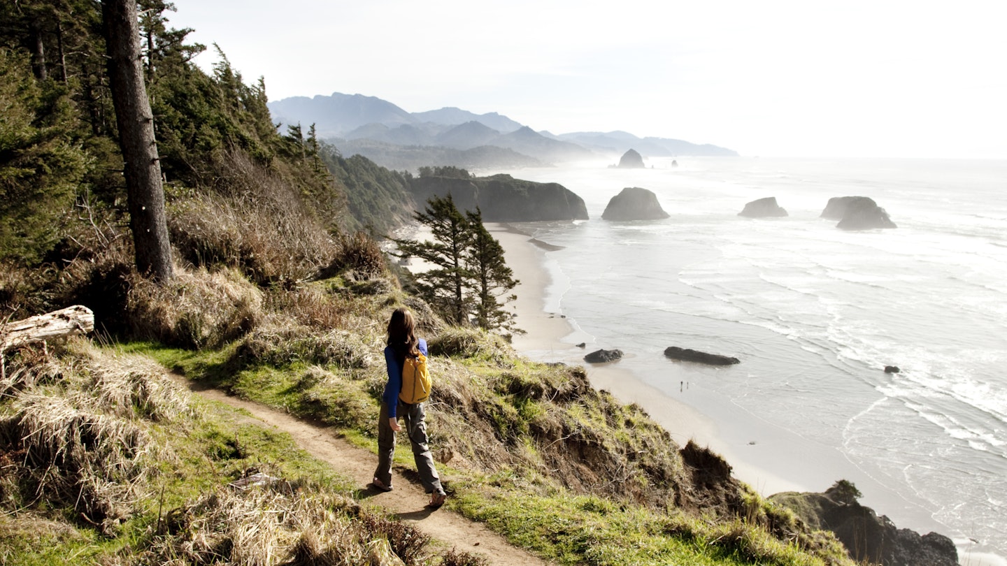 Female hiker walking along a secluded coastline path in Ecola State Park.