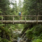 A female hiker walking across a log bridge in the Olympic National Park. 