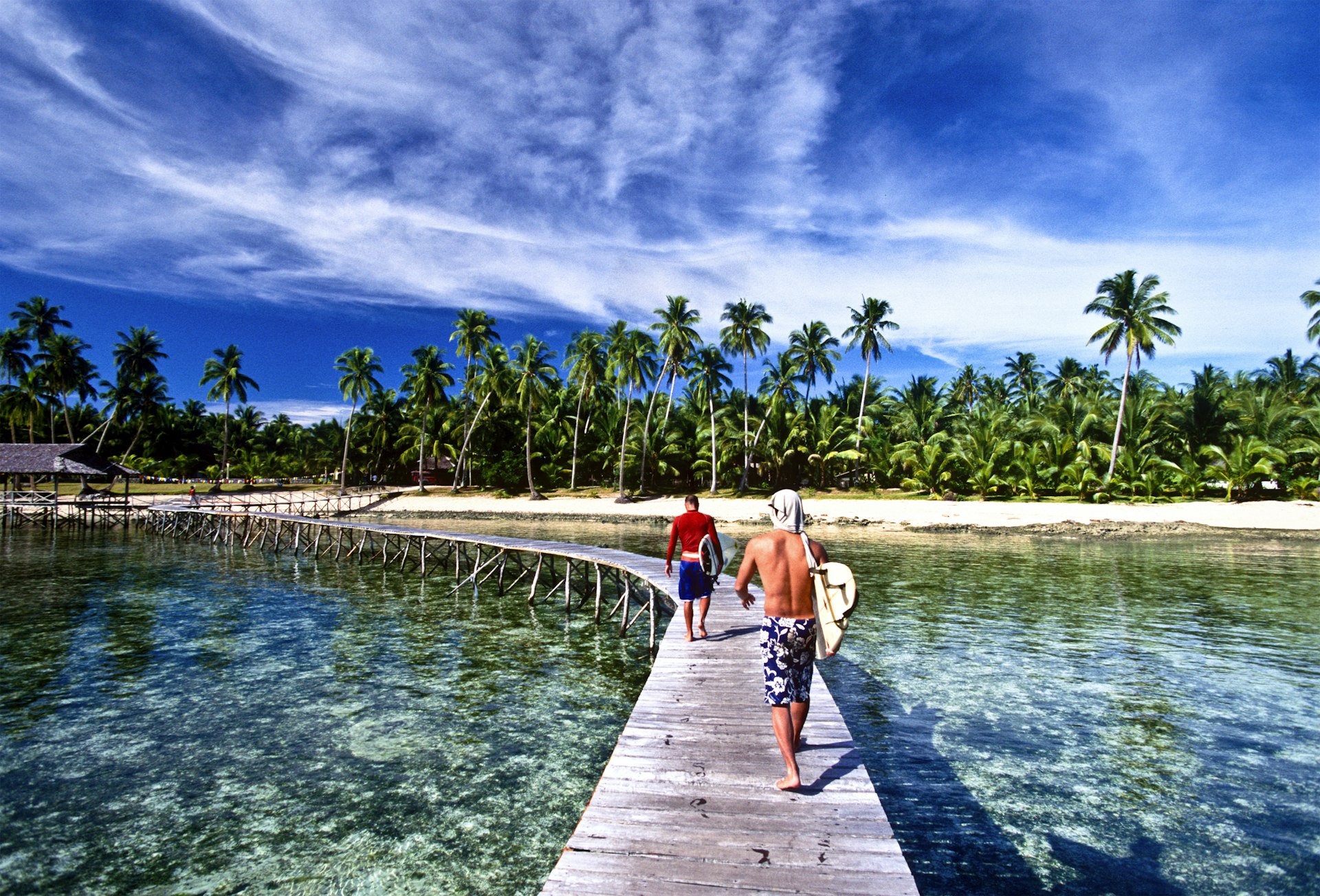 Two surfers walk along a wooden pier on Siargao Island, the Philippines