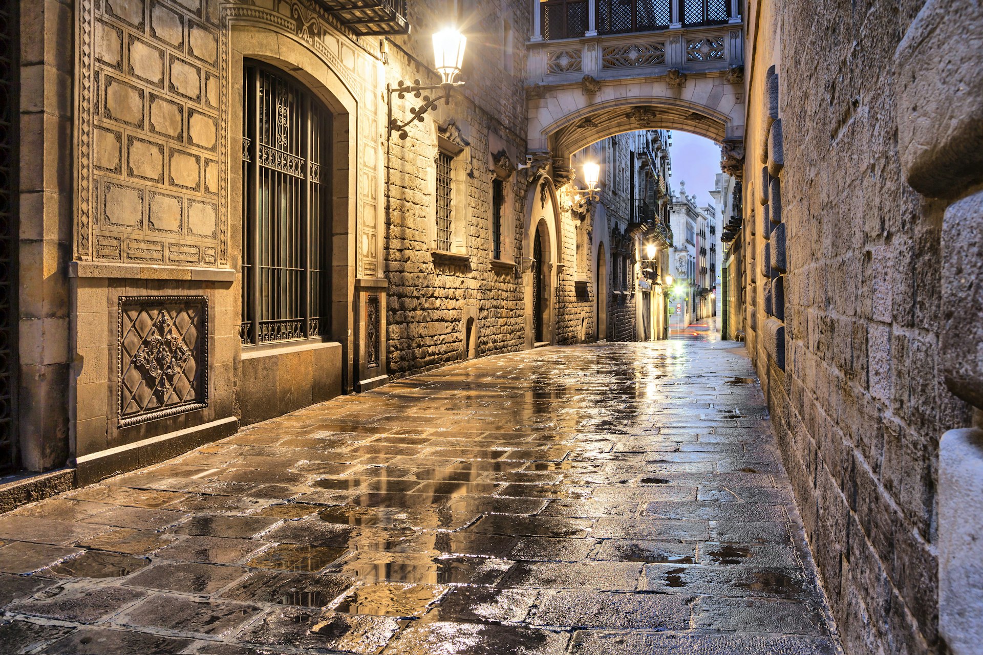 Narrow empty stone street in the Gothic quarter, with a stone bridge passing overhead.  