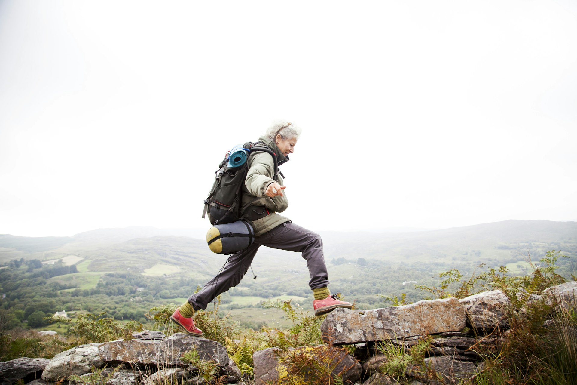 An older woman jumps across rocsk in the mountains of Ireland