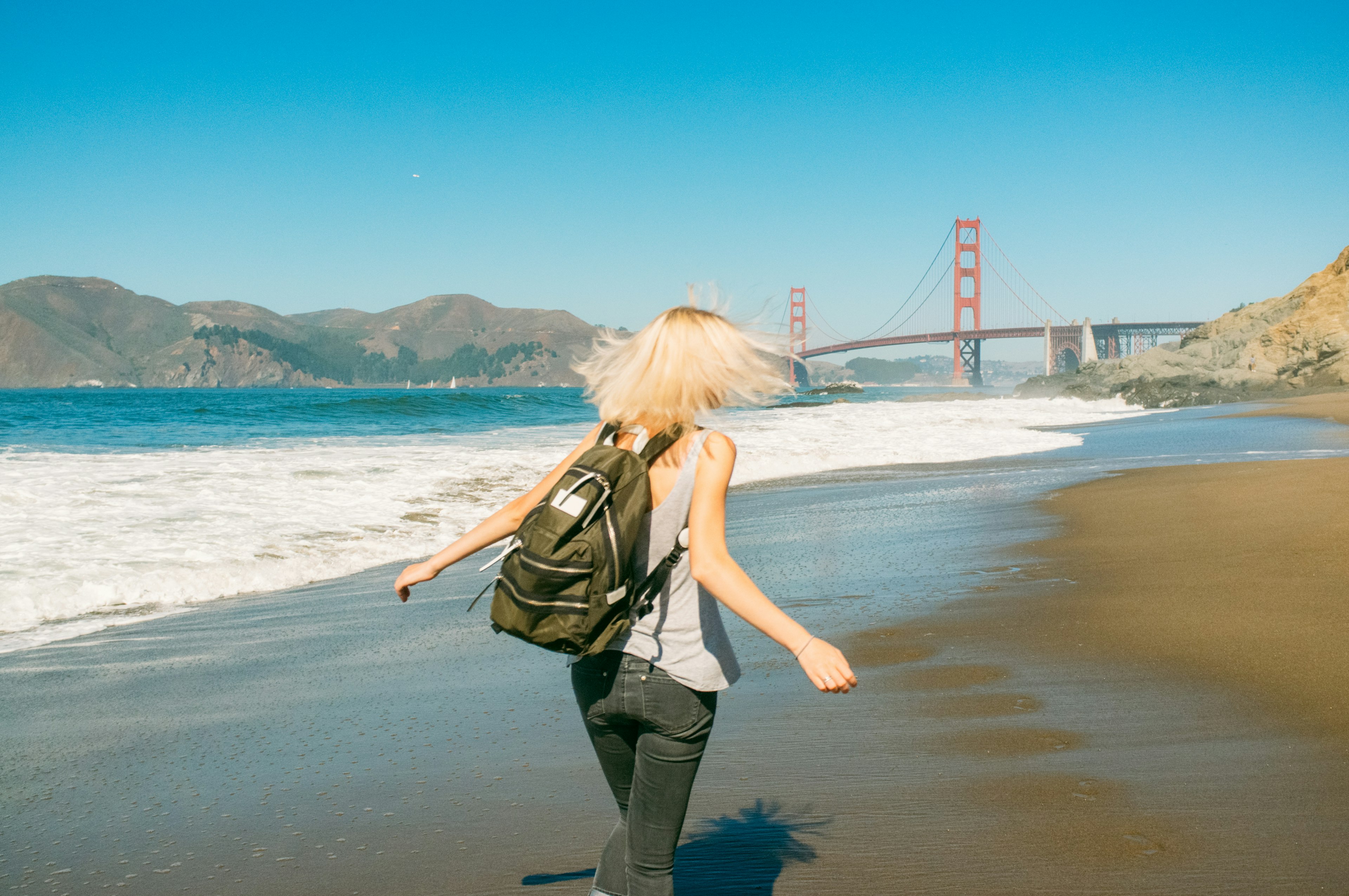 Woman walking on the shore with Golden Gate Bridge in the background.