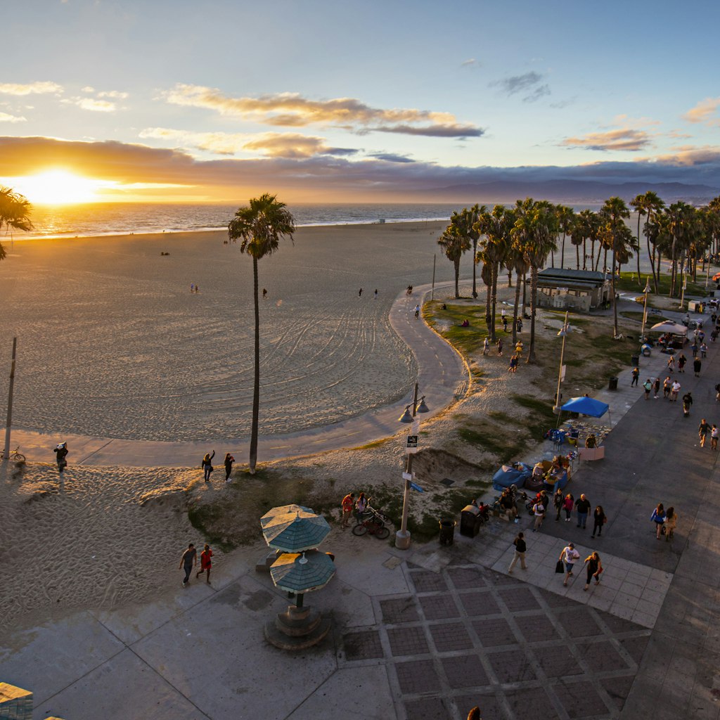 High angle view of Venice beach during sunset. Tourists are walking on footpath by ocean. Shot of beautiful nature and people is taken from above.