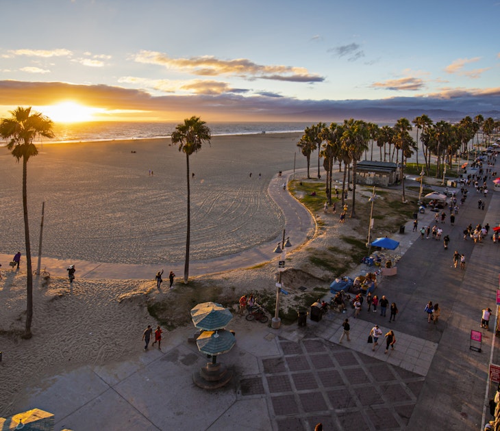 High angle view of Venice beach during sunset. Tourists are walking on footpath by ocean. Shot of beautiful nature and people is taken from above.