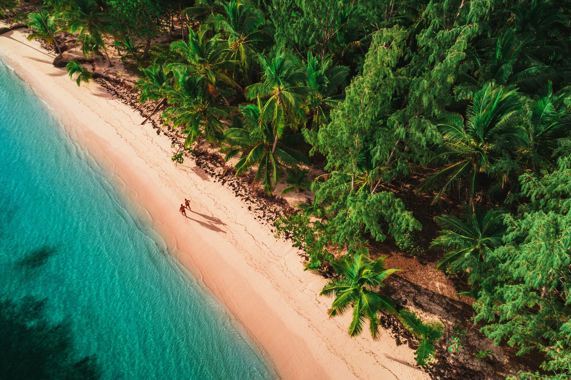 Aerial view of two people walking down a tropical island beach