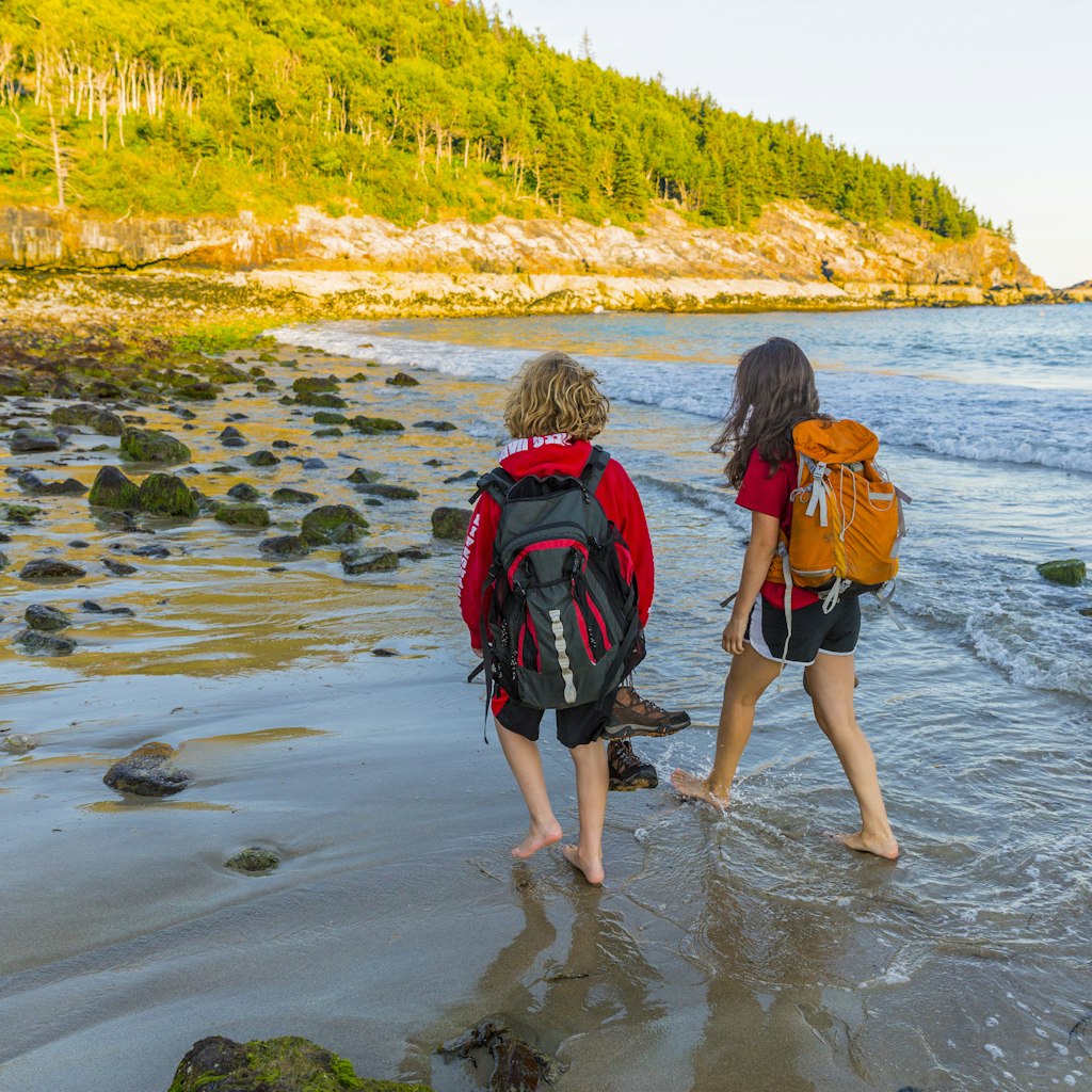 Teenage boy and girl walking on the beach barefoot in Acadia National Park.