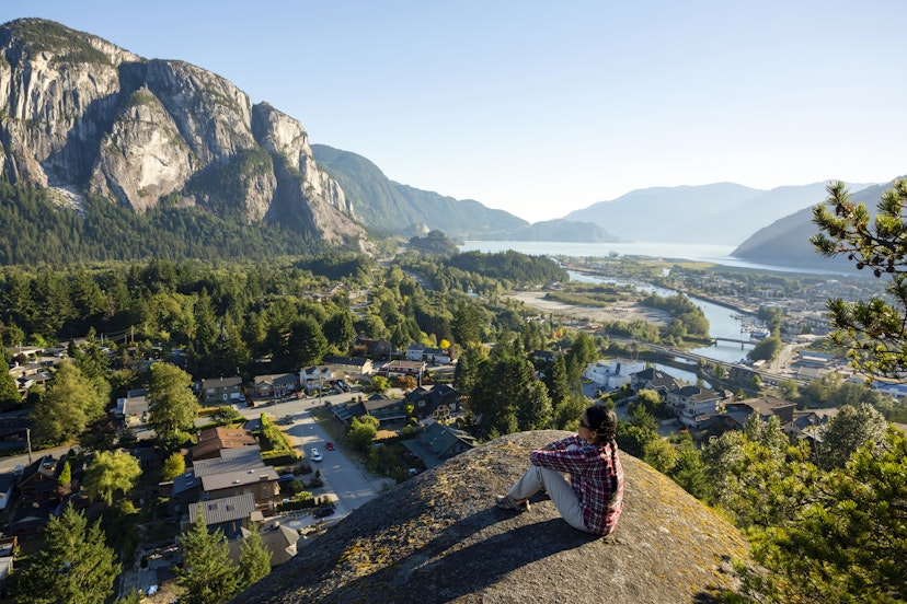 Woman sitting on the edge of a cliff at Smoke Bluffs Park overlooking Howe Sound and the Stawamus Chief in Squamish.