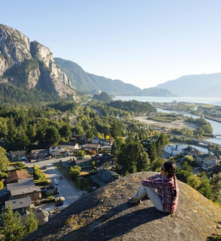 Woman sitting on the edge of a cliff at Smoke Bluffs Park overlooking Howe Sound and the Stawamus Chief in Squamish.