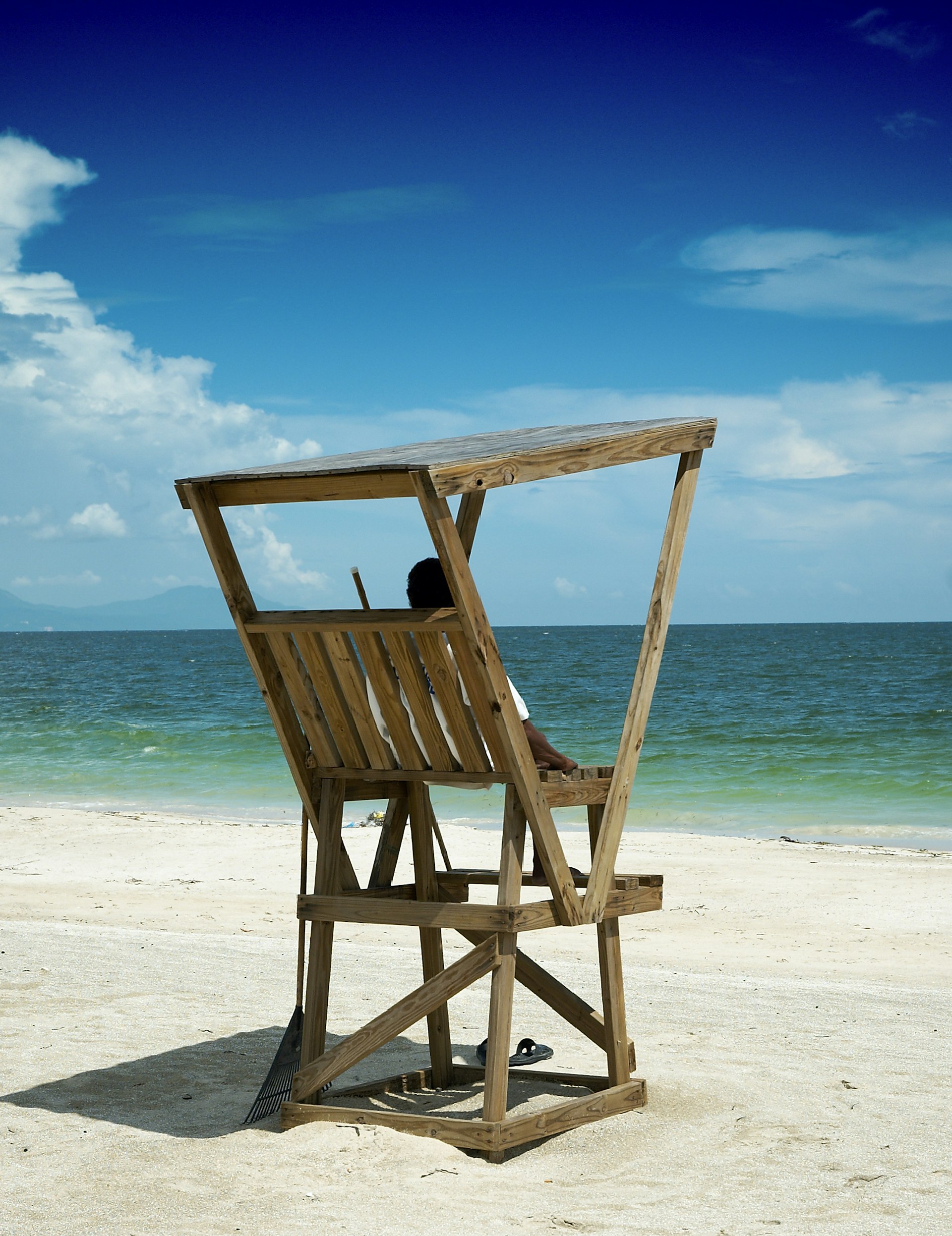 A person stares out to the ocean while sitting in a wooden lifeguard hut at Hellshire Beach in Jamaica