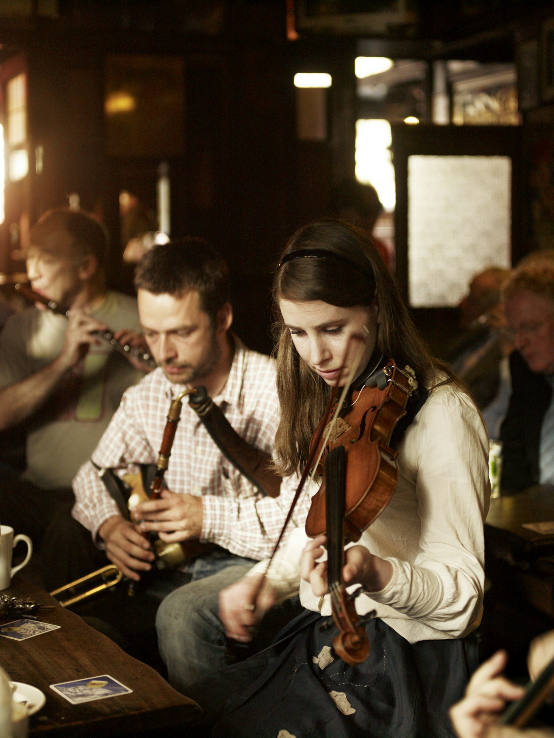 A woman playing the violin and a man playing the uilleann pipes in a pub