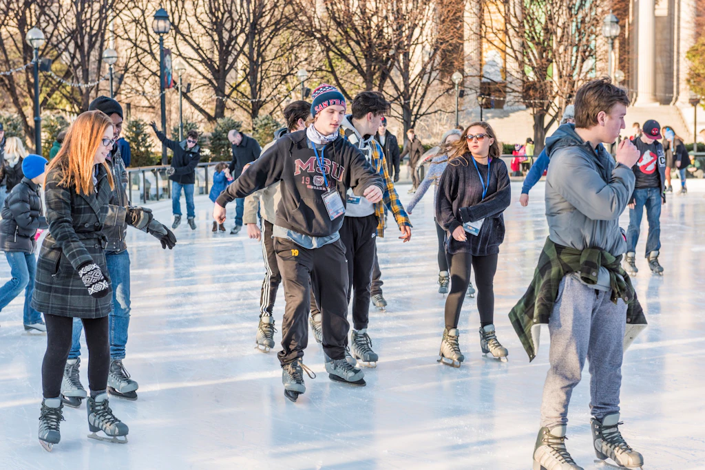 Art Sculpture Garden ice rink Ice skaters in warm weather gear, including hats and gloves, skate across the ice rink in the National Gallery of Art Sculpture Garden in Washington DC with leafless trees in the background.