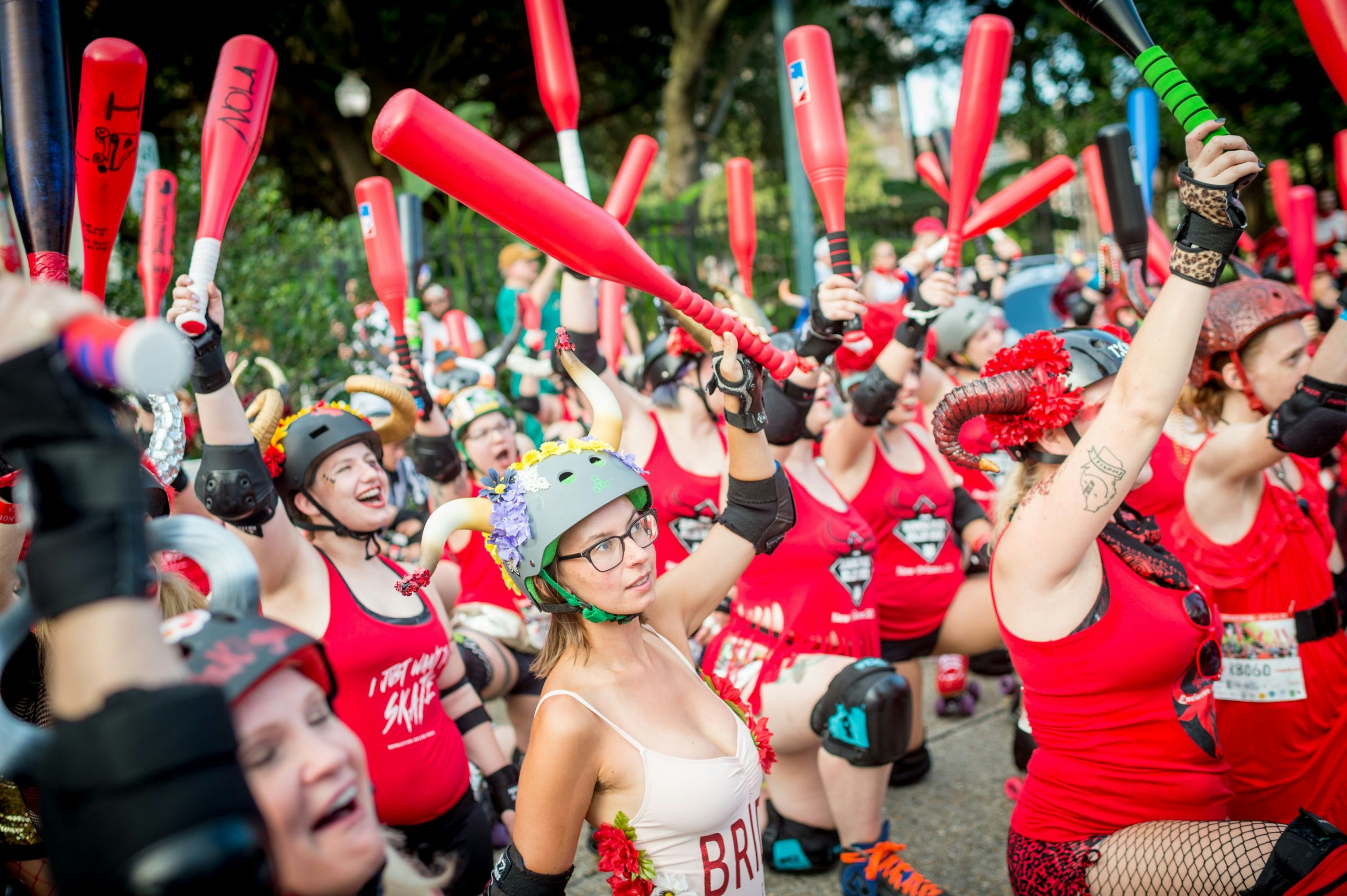 A large group of women, some wearing helmets with horns hold up red plastic bats while wearing roller skates during the annual Running of the Bulls in New Orleans. 