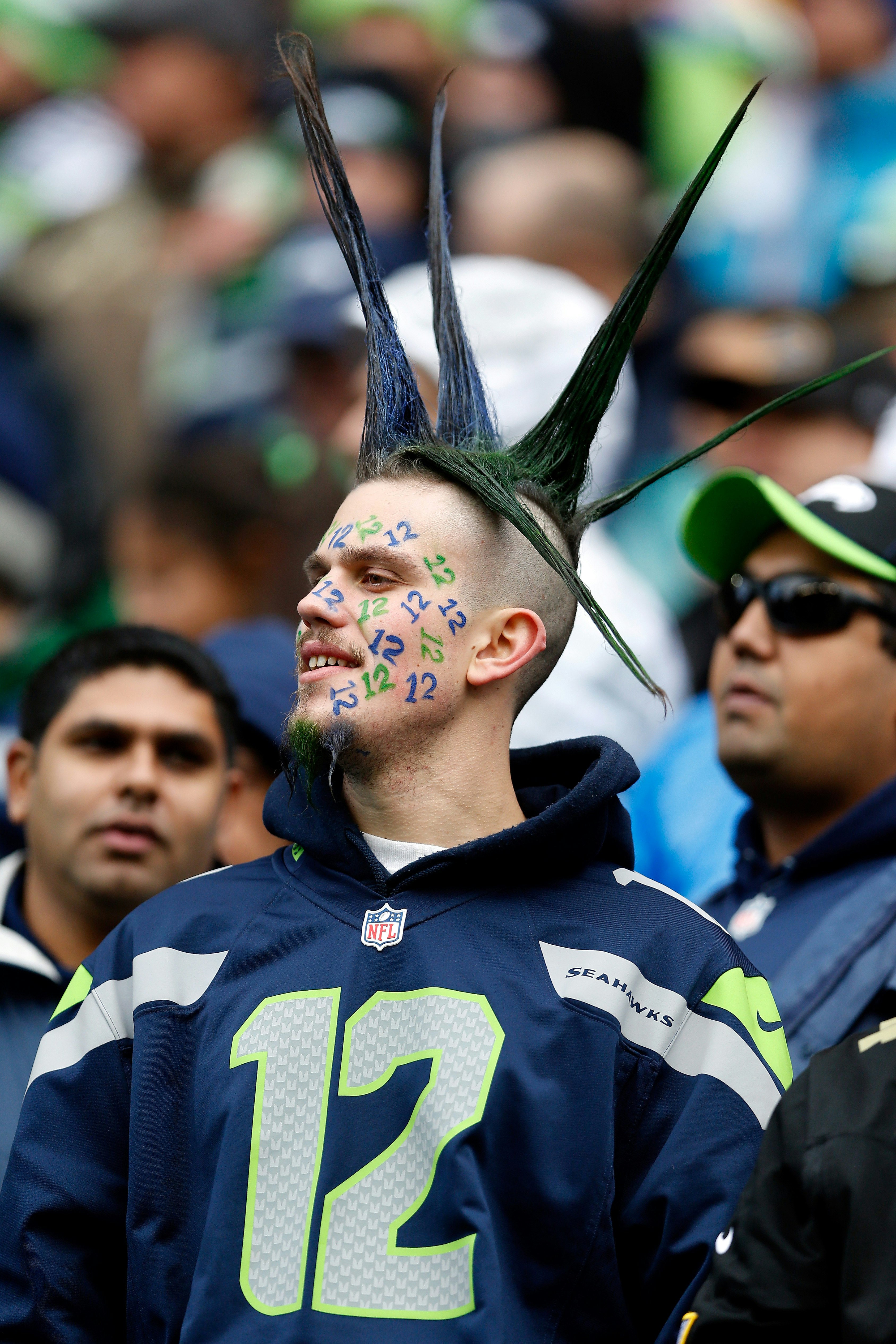 A Seattle Seahawks fan looks on against the Green Bay Packers. His hair is spiked and his face is covered with blue and green number 12s.