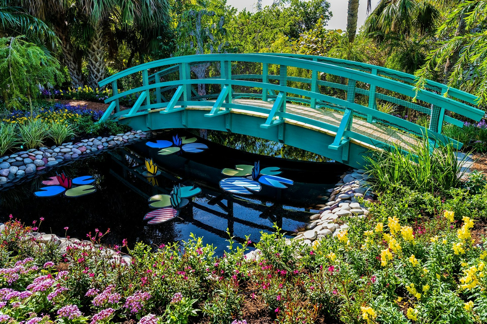 A blue bridge over a pond with flowers floating in it