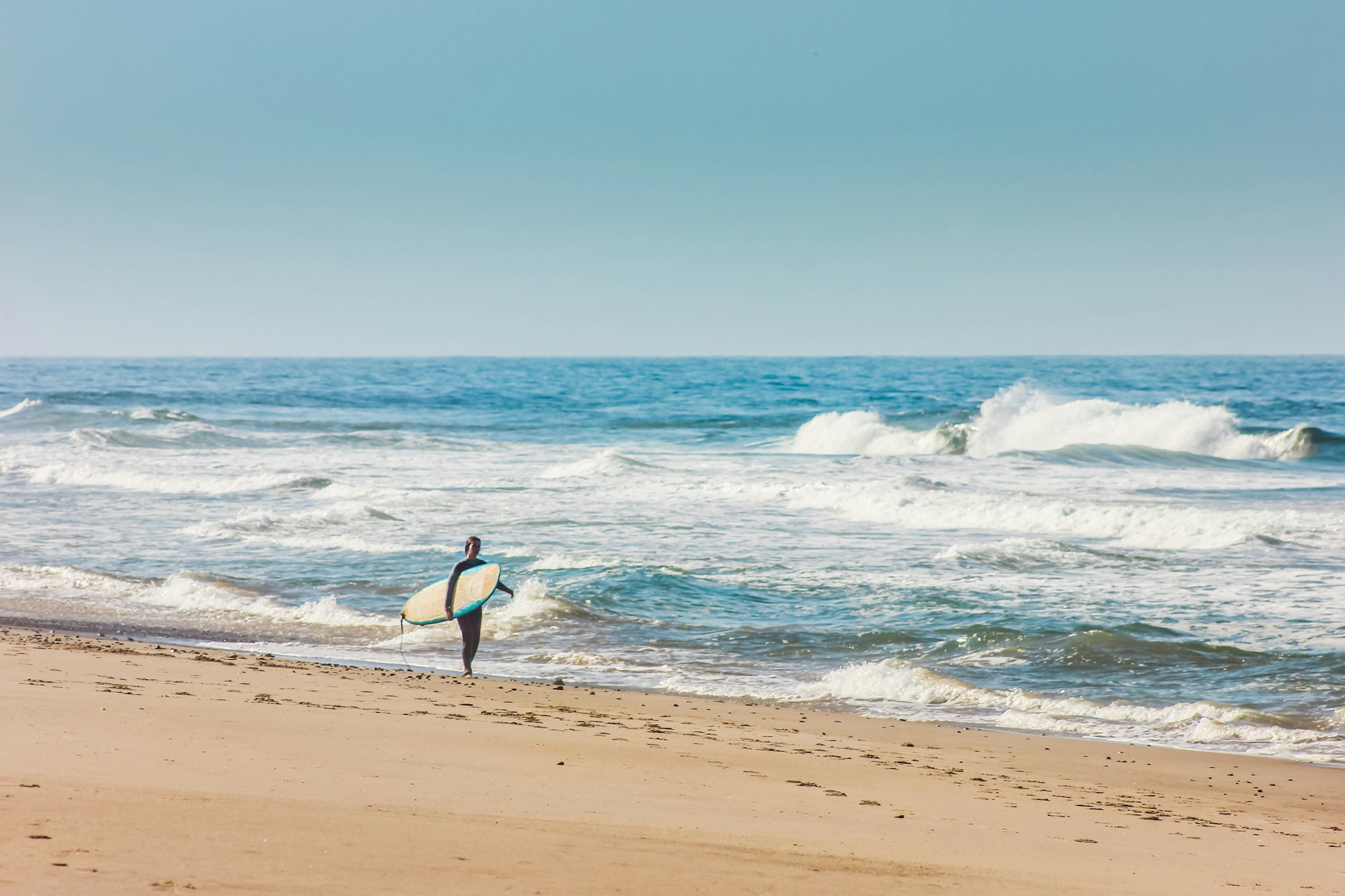 Young woman on the beach carrying a surfboard in Malibu