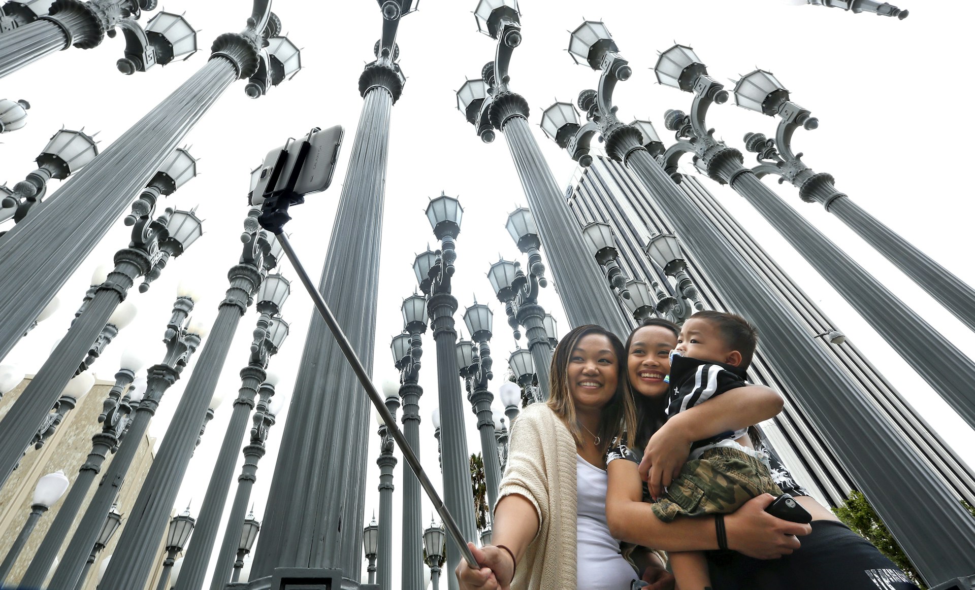 Three people taking a selfie in front of the Urban Light installation at the Los Angeles County Museum of Art