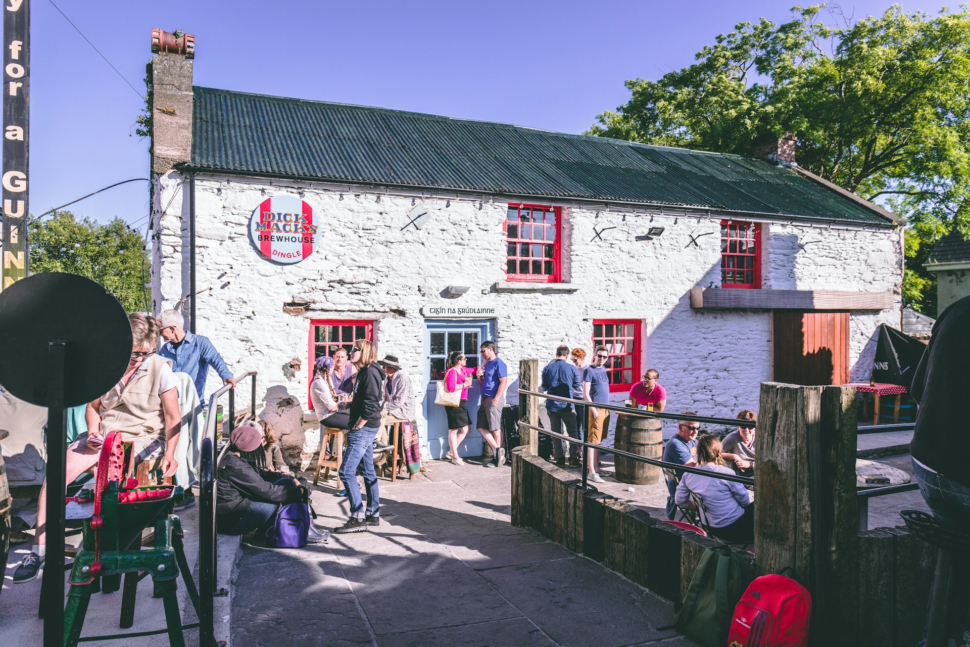 People drinking outside a pub made of white-washed stone on a sunny day.