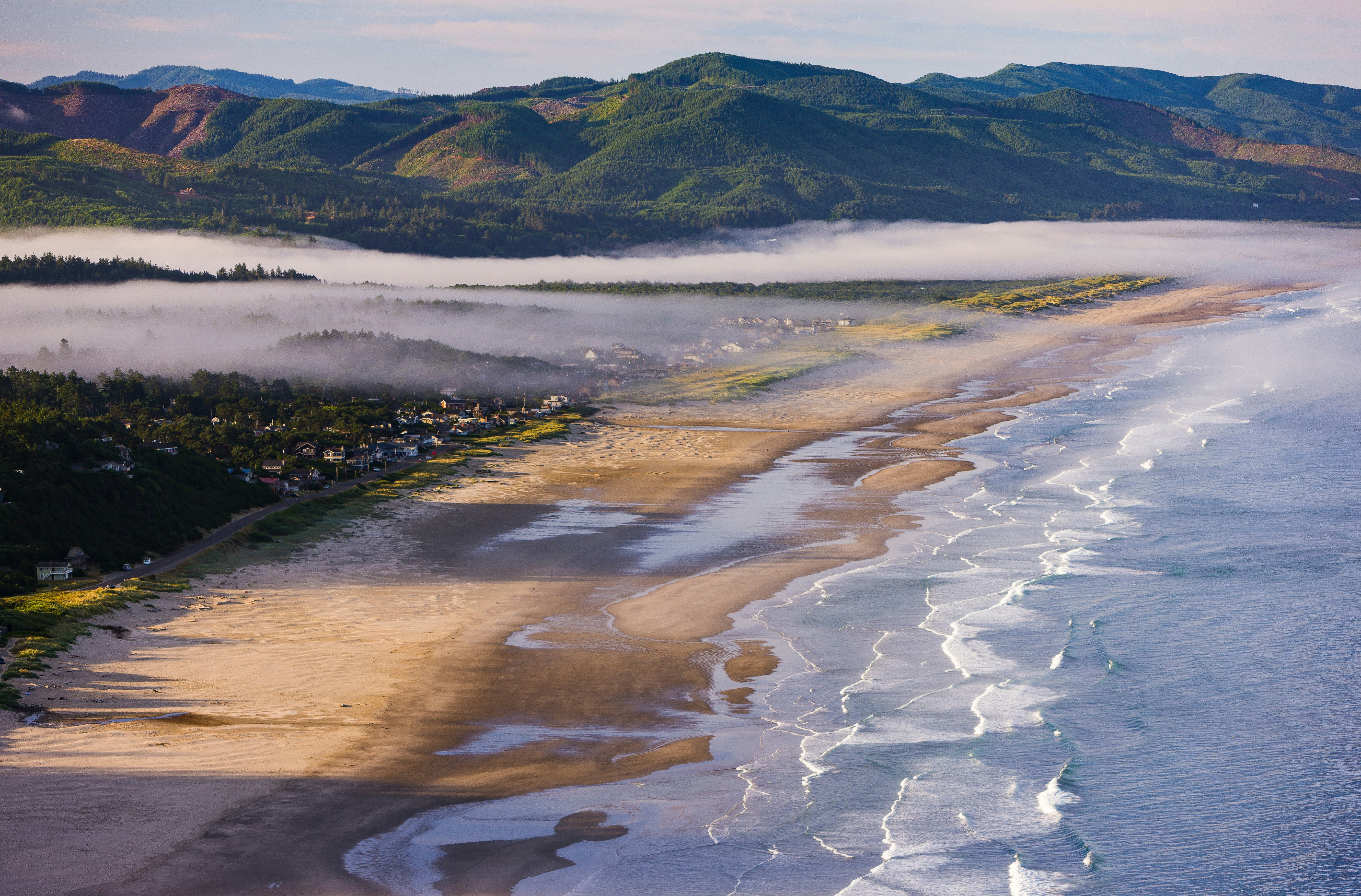 A long beach backed by hills that are shrouded in morning mist