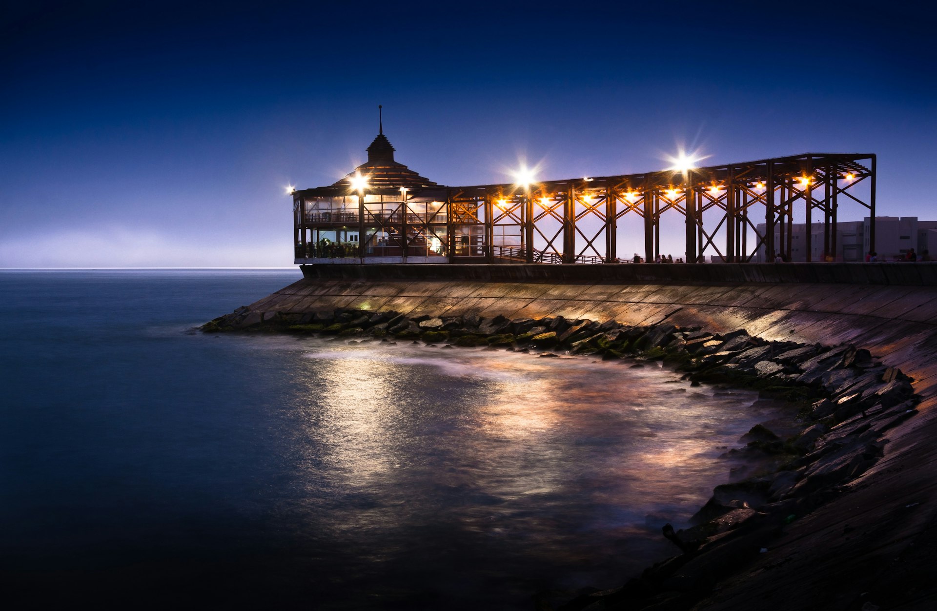A pier is light up at night against a deep purple sky. 