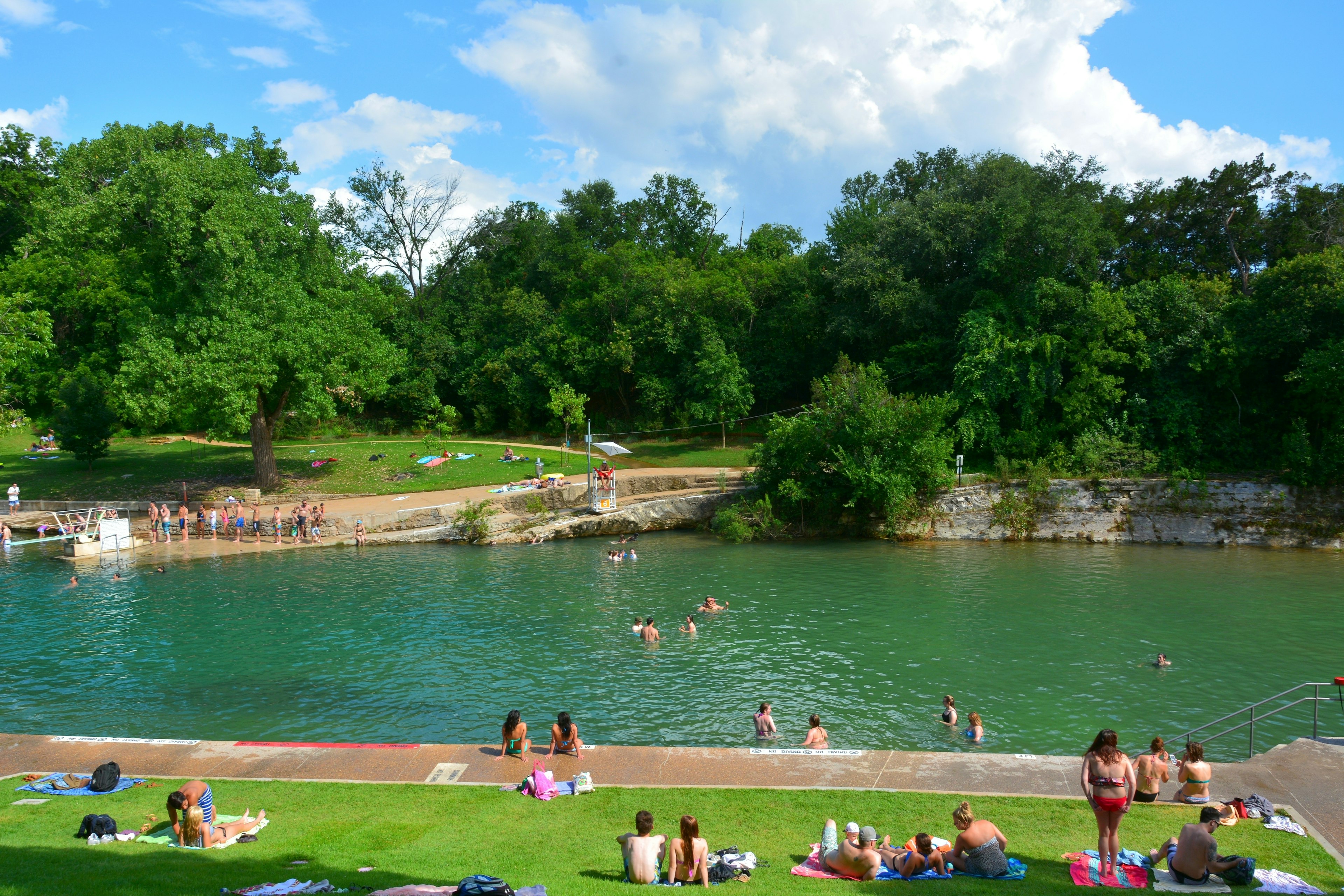 Outdoor springs. People line up to use a diving board; others swim or lounge by the side