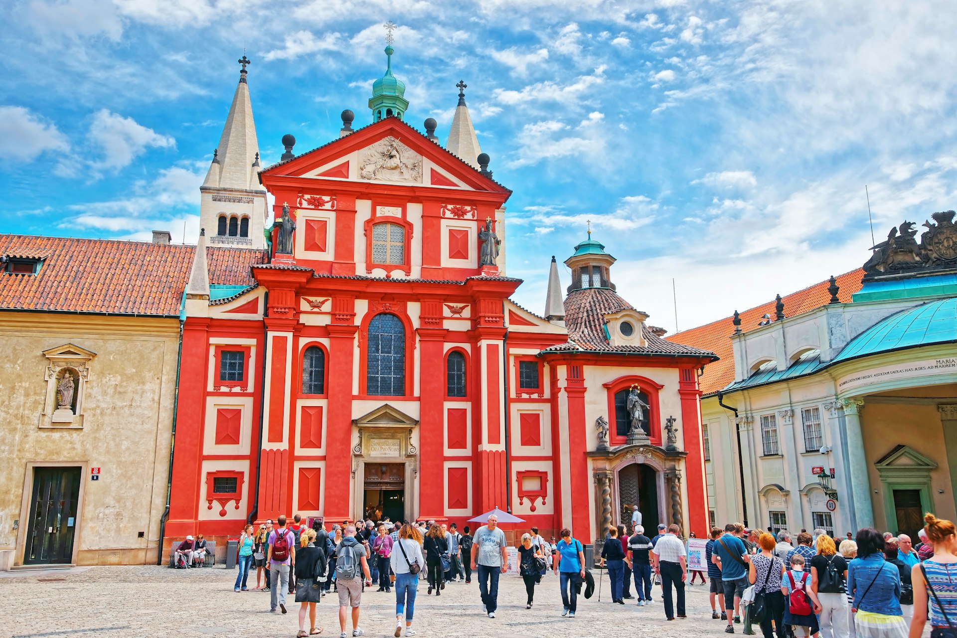 Tourists milling around the red facade of St George Basilica in Prague Castle in the Czech Republic on a sunny June day