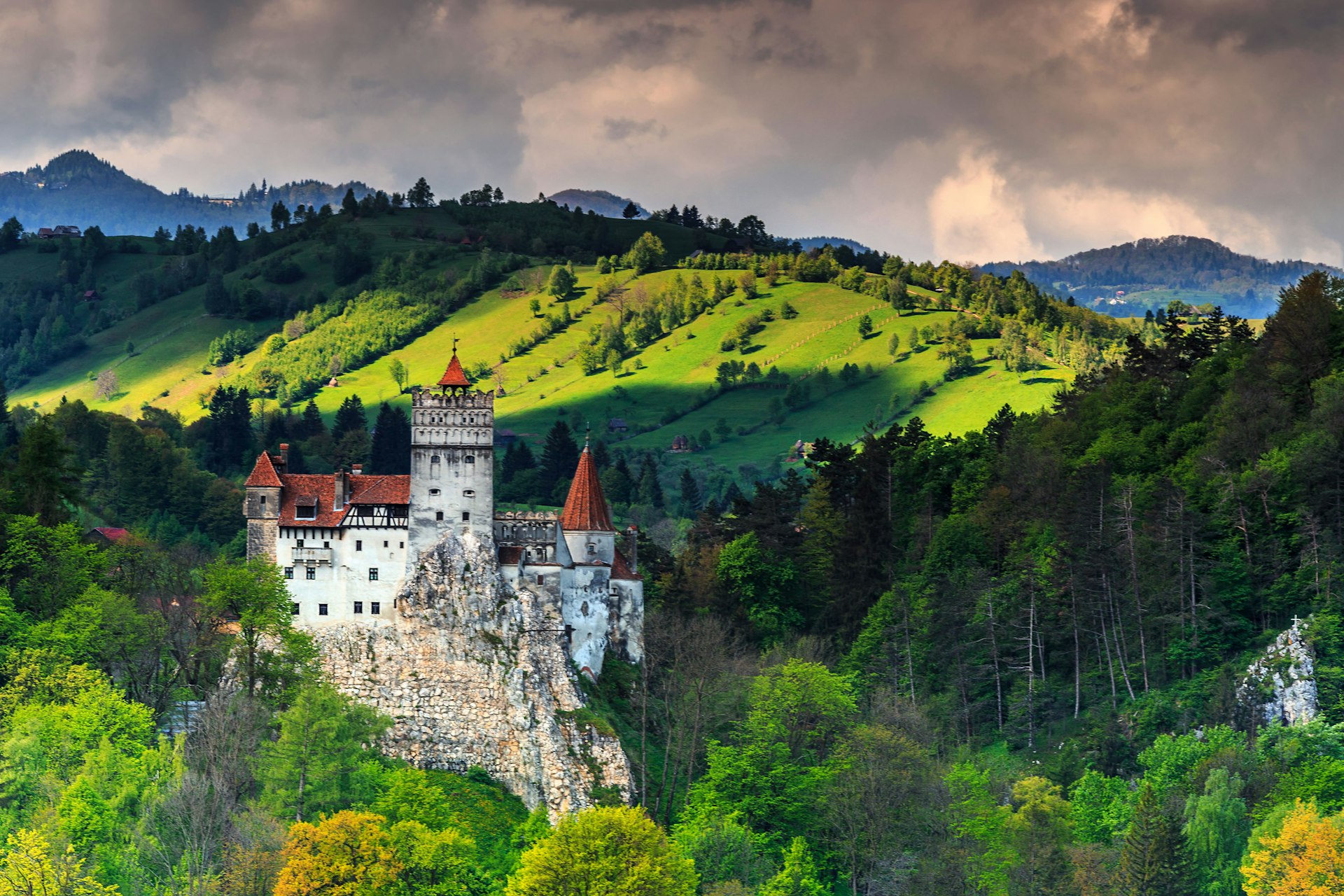A castle on a hill stands in front of a lush mountainous area. 