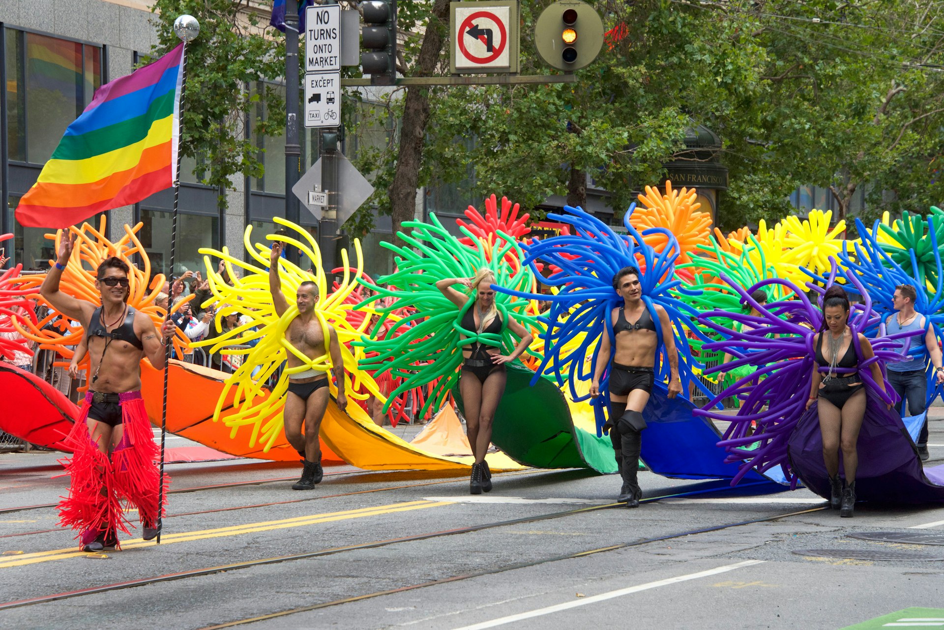 People take part in a parade wearing pants and shoes with colorful balloons attached to them