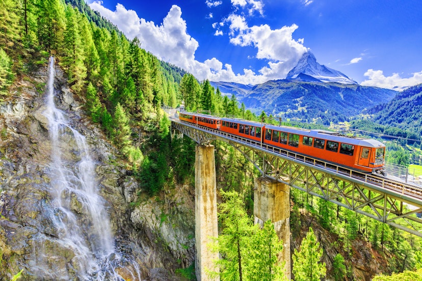Gornergrat tourist train passing over the Findelbach Bridge with a waterfall and the Matterhorn in the background.