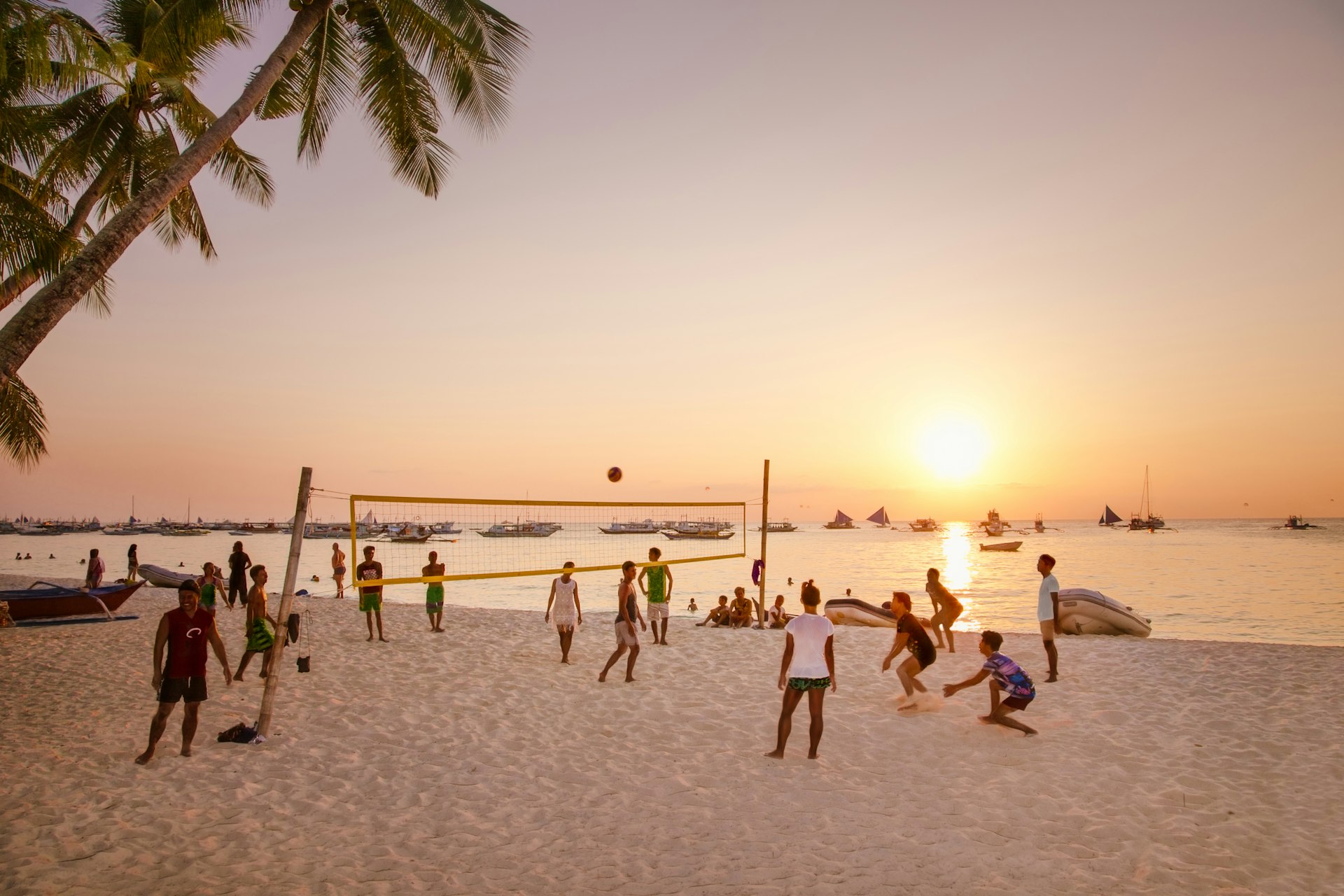A group of people play volleyball as the sun sets at White beach, Boracay Island.