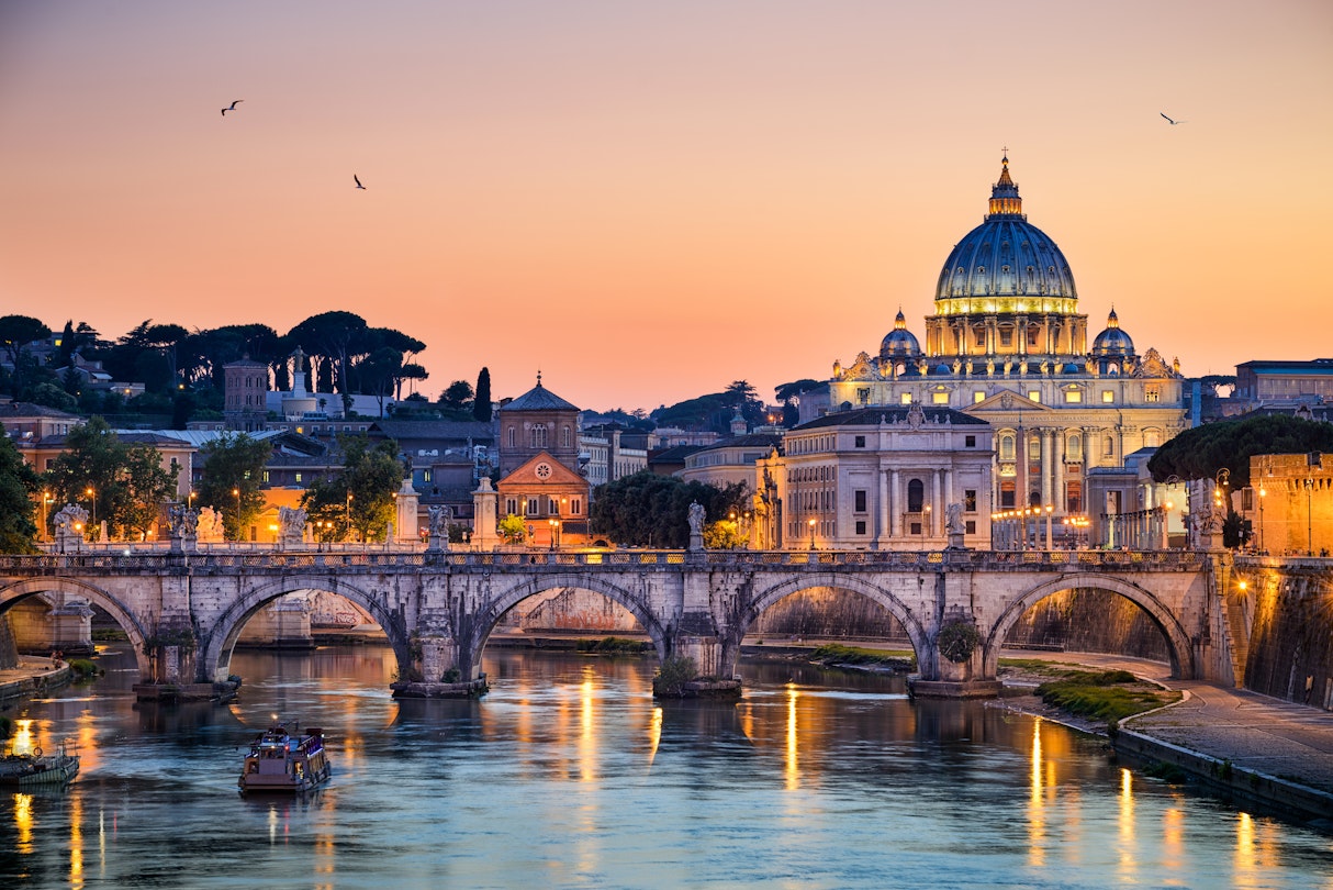 With the ancient Sant'Angelo bridge and the St. Peter's Basilica of Vatican lined up in front of a sunset sky.