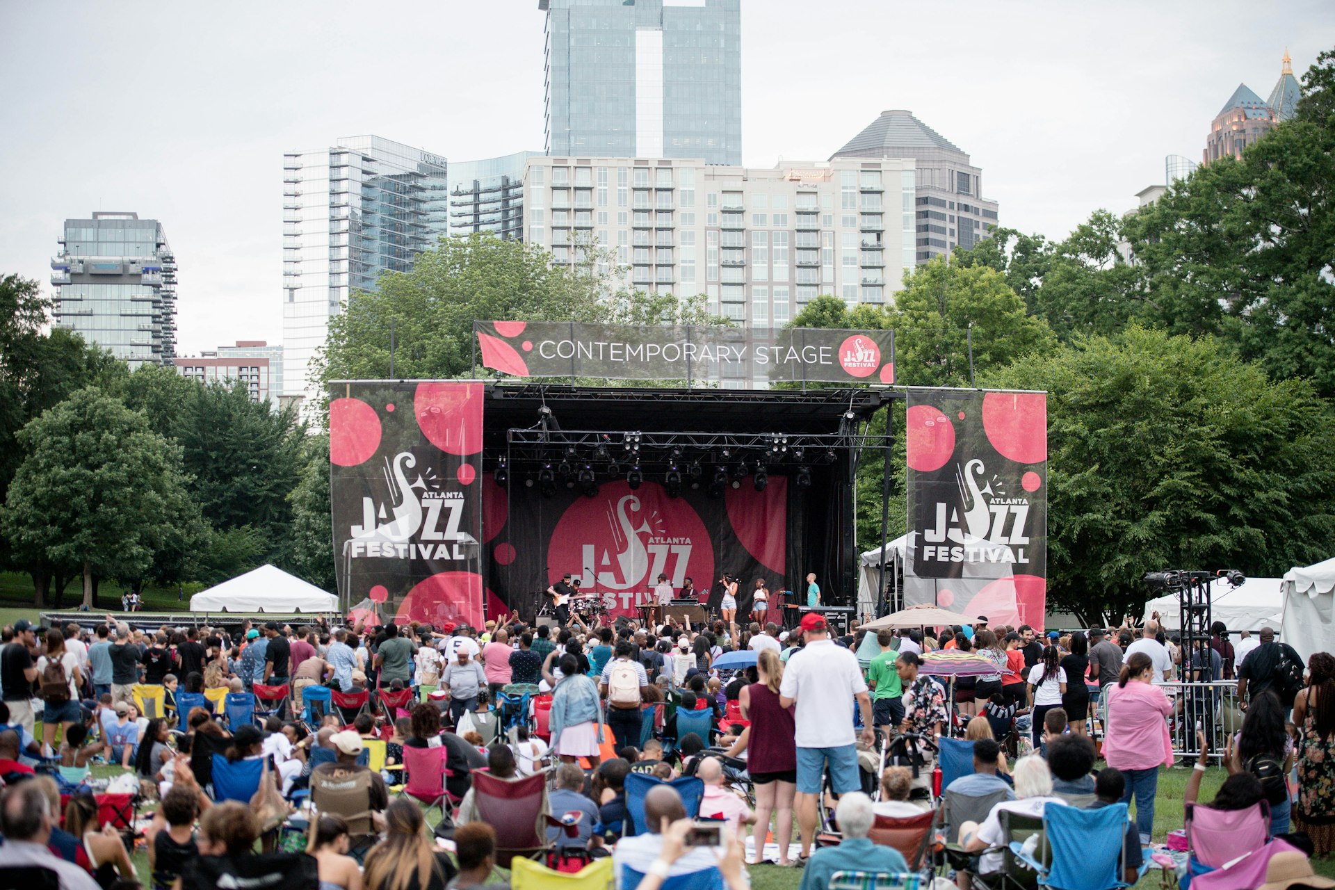 A large group of people sit or stand on the grassy lawn facing the stage during the Atlanta Jazz Festival. This picture was taken in 2018.