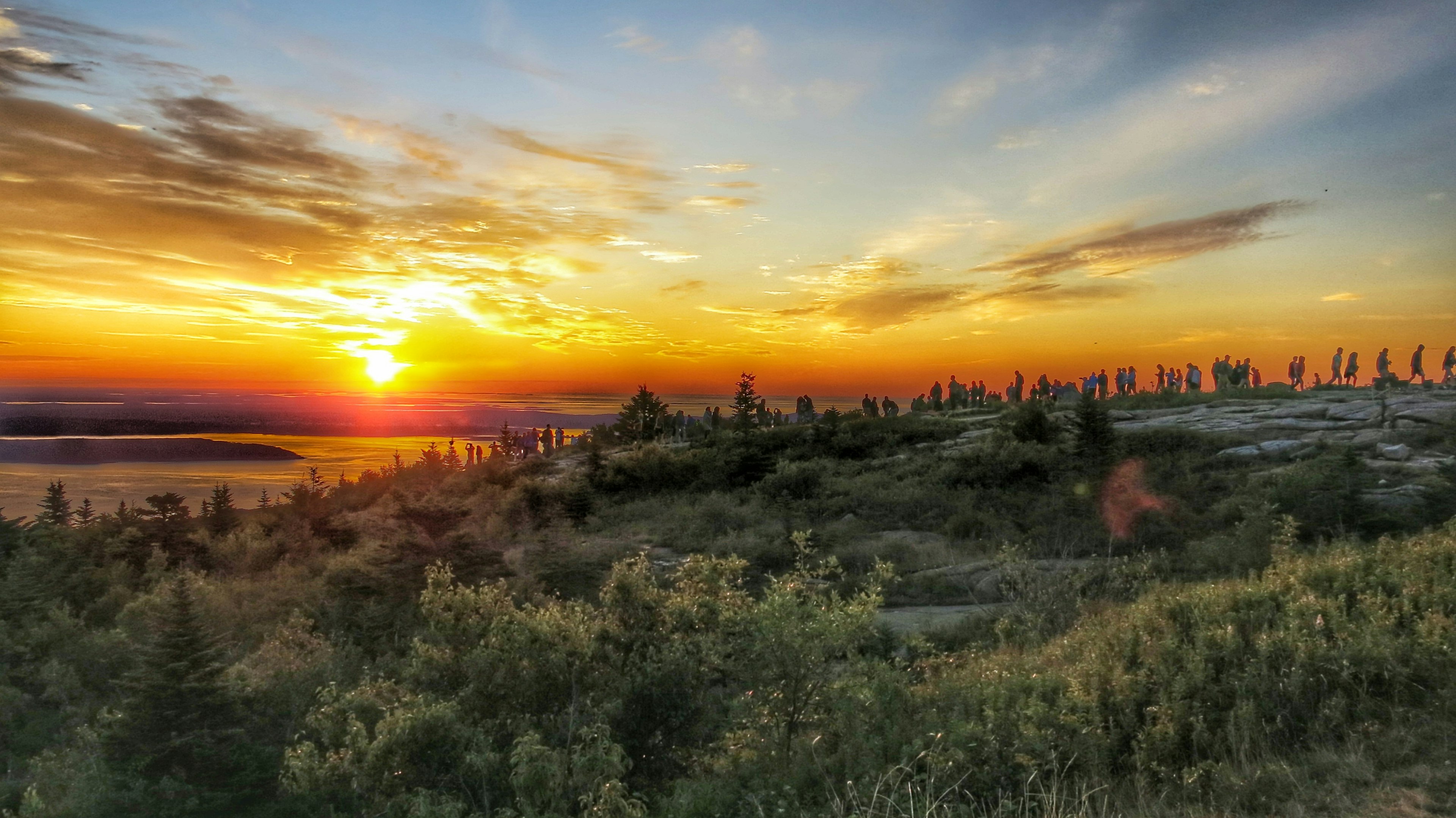 A row of people standing at the summit of Cadillac Mountain as the sun rises