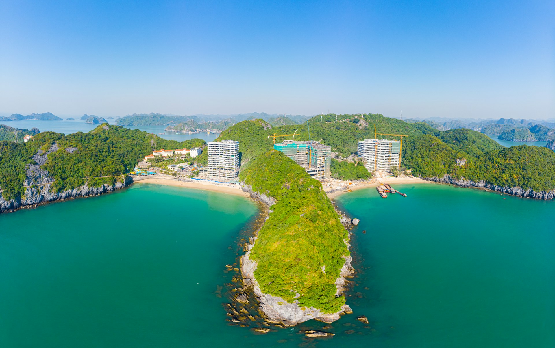 An aerial view of two of Cat Ba island's beaches. New building construction is being done on the beach. The water and sky are both a lovely shade of blue.