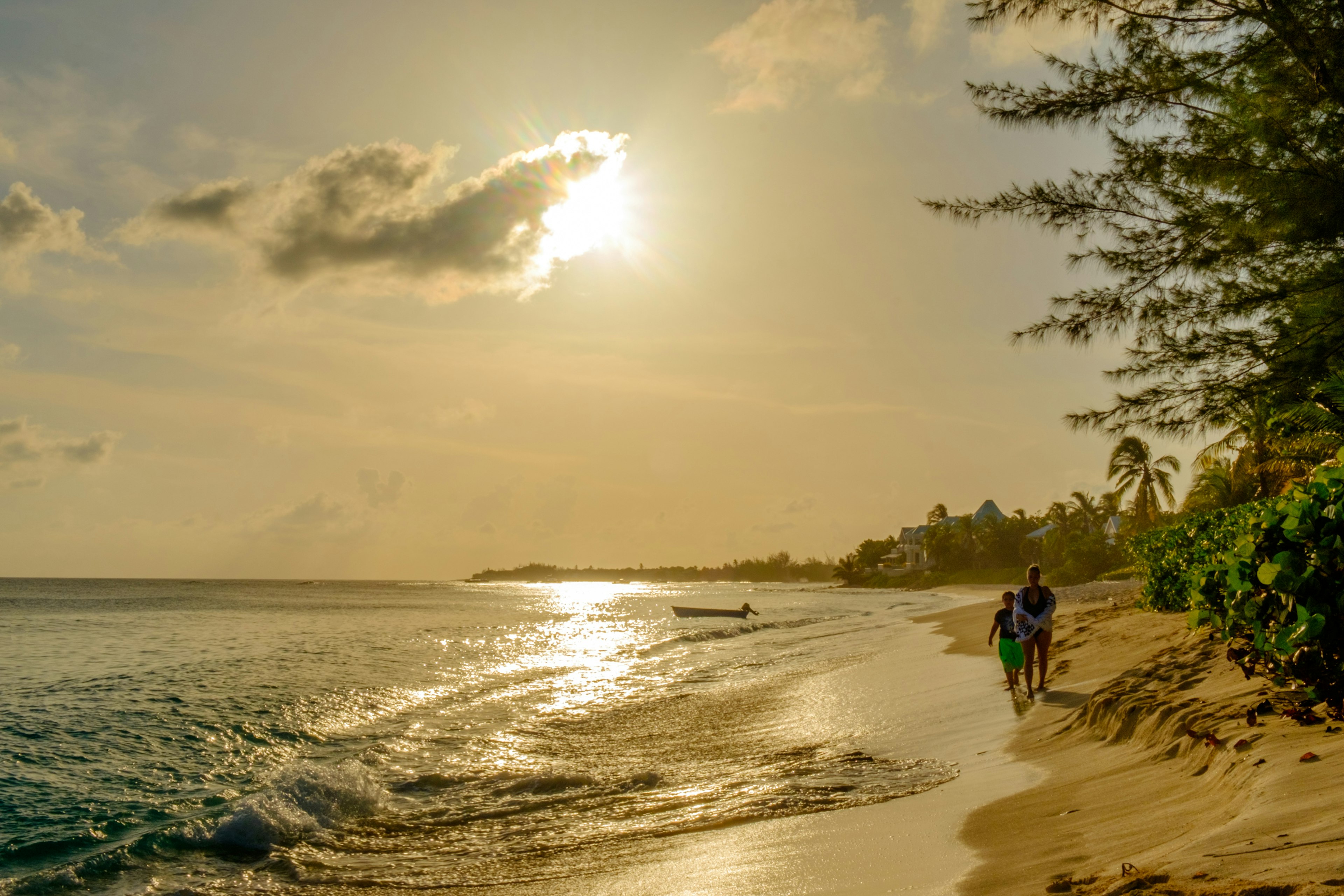 A couple strolls at sunset alongside the surf, sand and palm trees of a beach