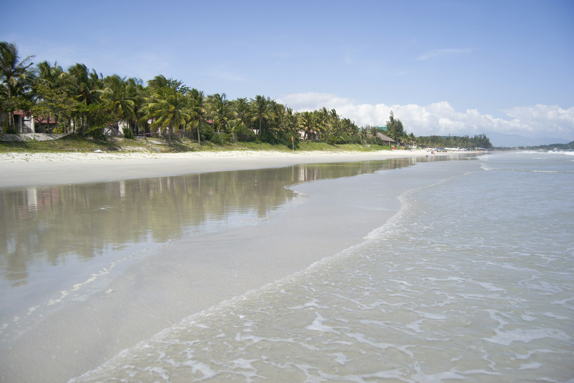 A view of Doc Let beach from the shallow waters. The beach has white sand and is backed by palm trees.