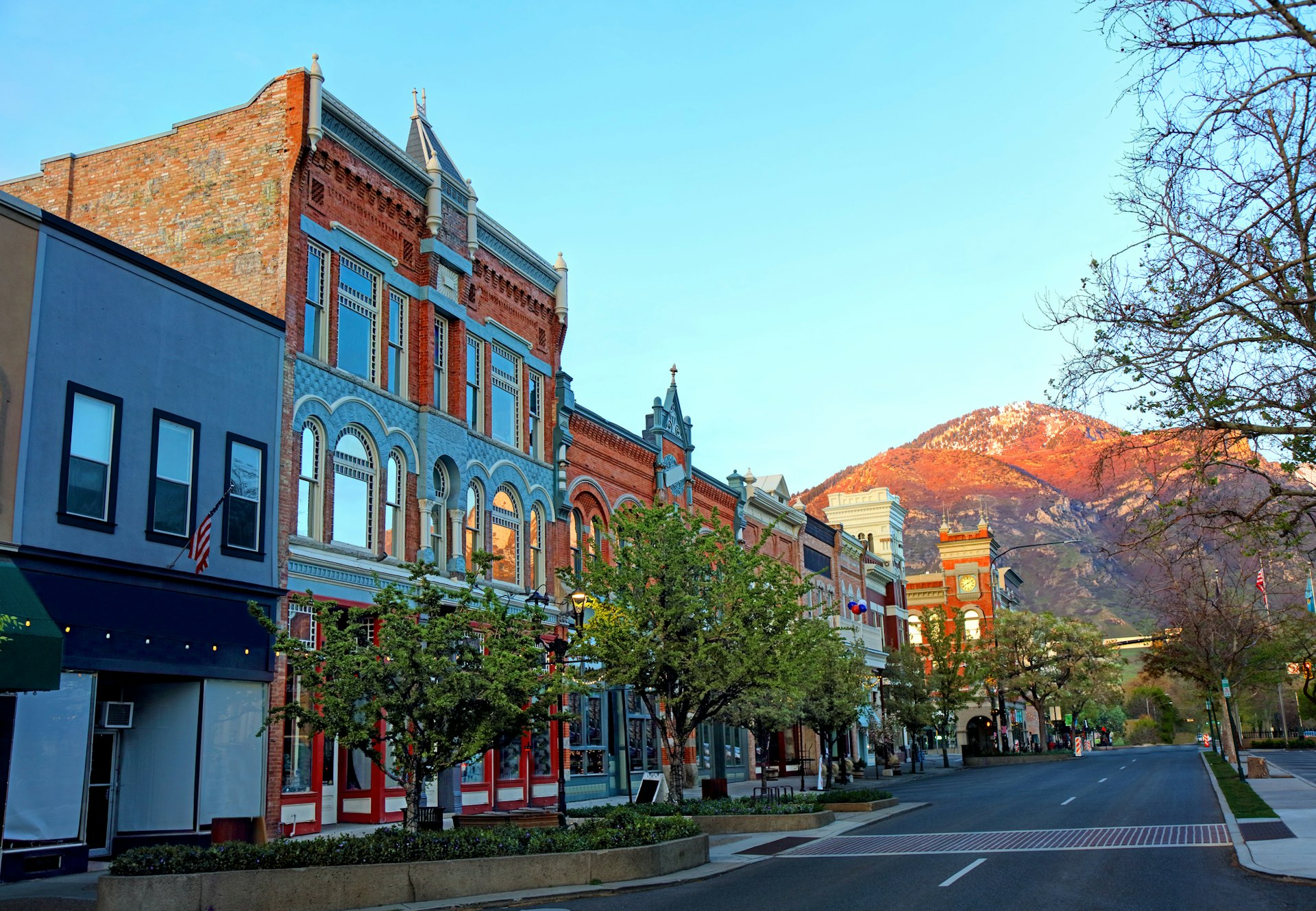 A strip of historic brick buildings lines a street in Provo, Utah in front of dramatic mountains