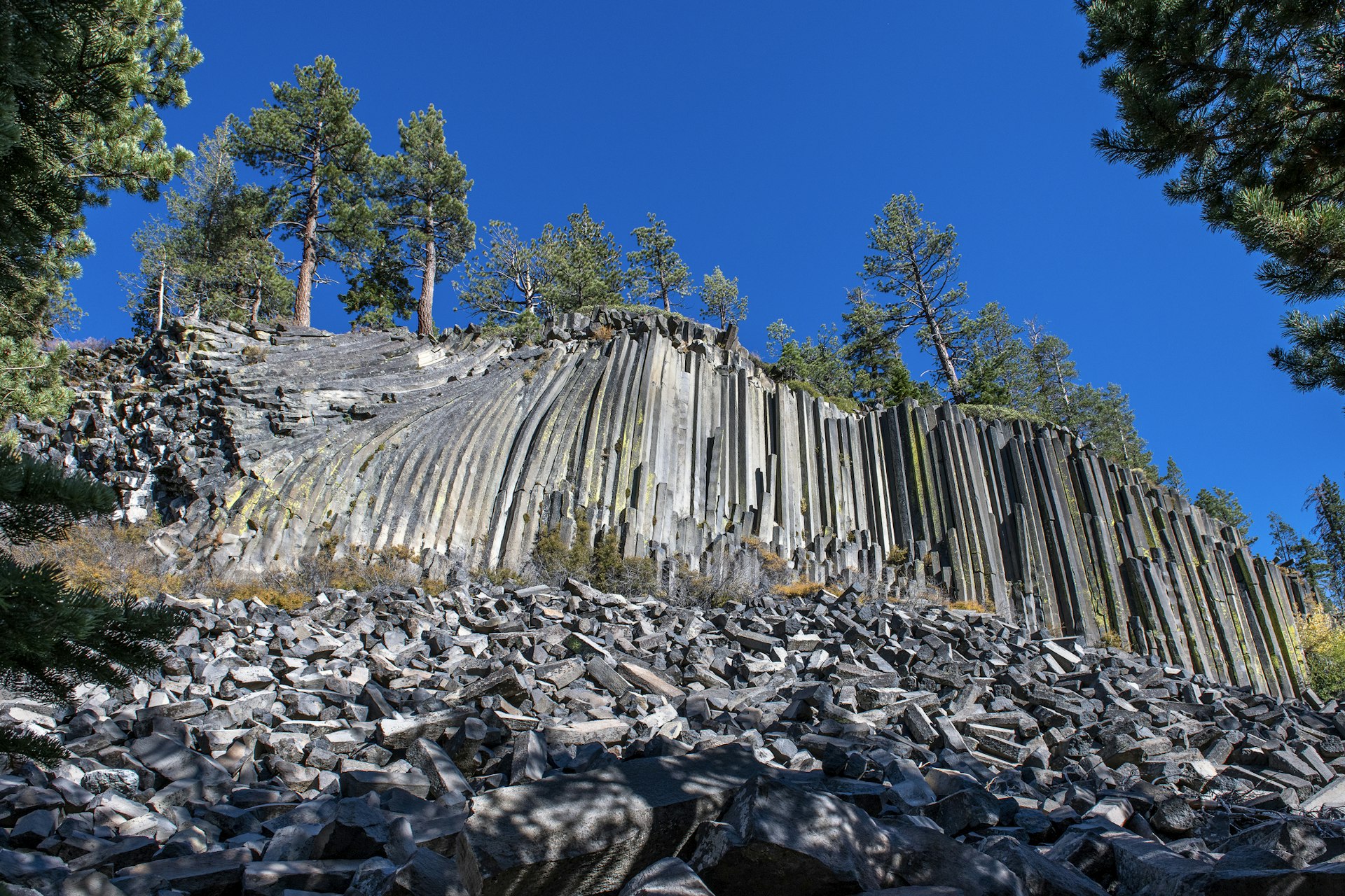 A cliff-face of basalt columns rises up from the rock-strewn ground at Devils Postpile National Monument