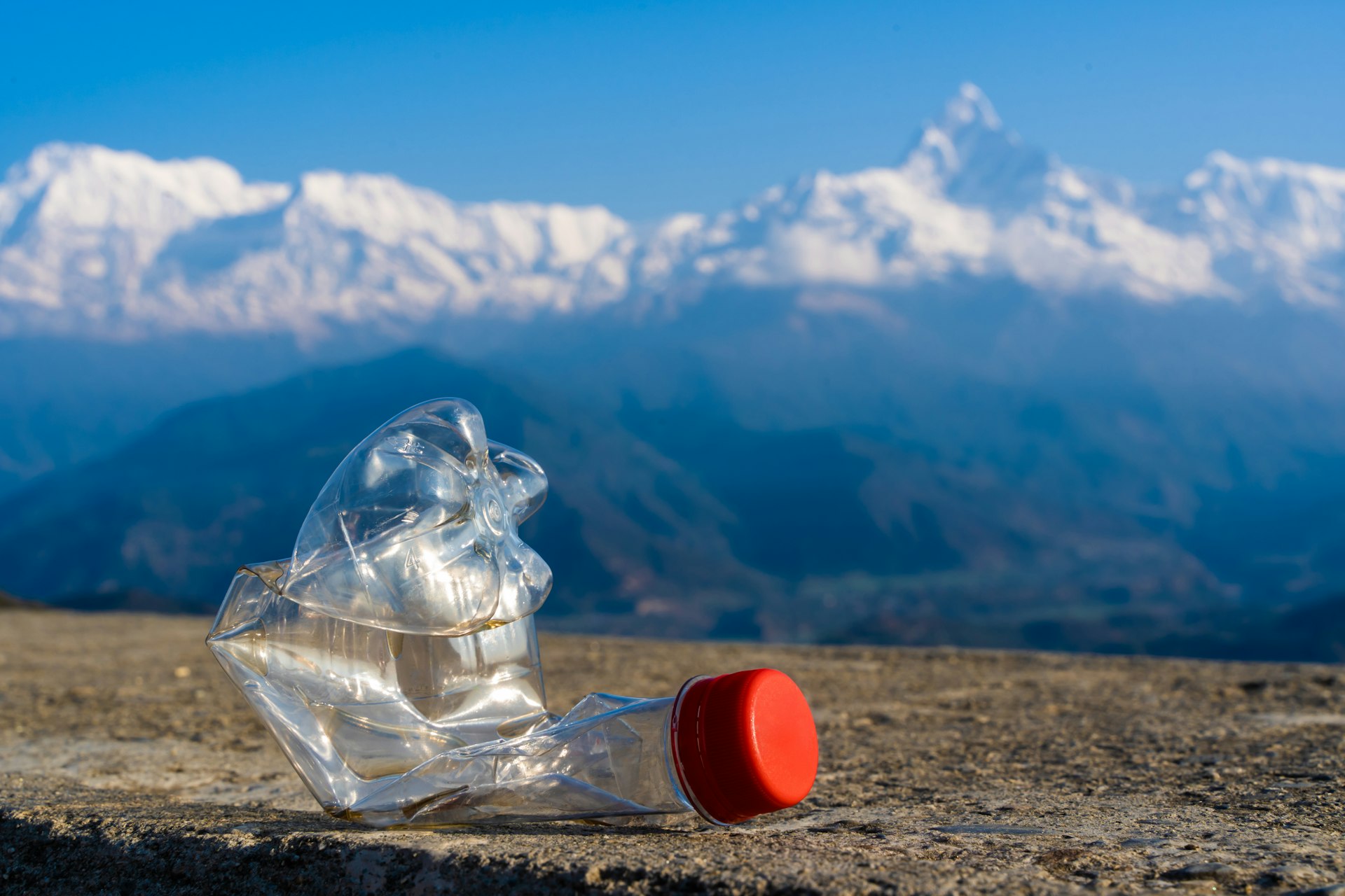árumpled empty plastic bottle on the background of a Annapurna mountain range, Himalaya. Environmental pollution in the tourist regions of the Himalaya mountains.