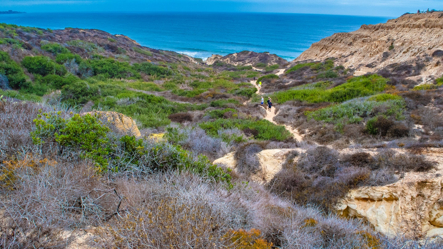 People walk along a sandy trail toward the beach during an early morning hike in La Jolla.