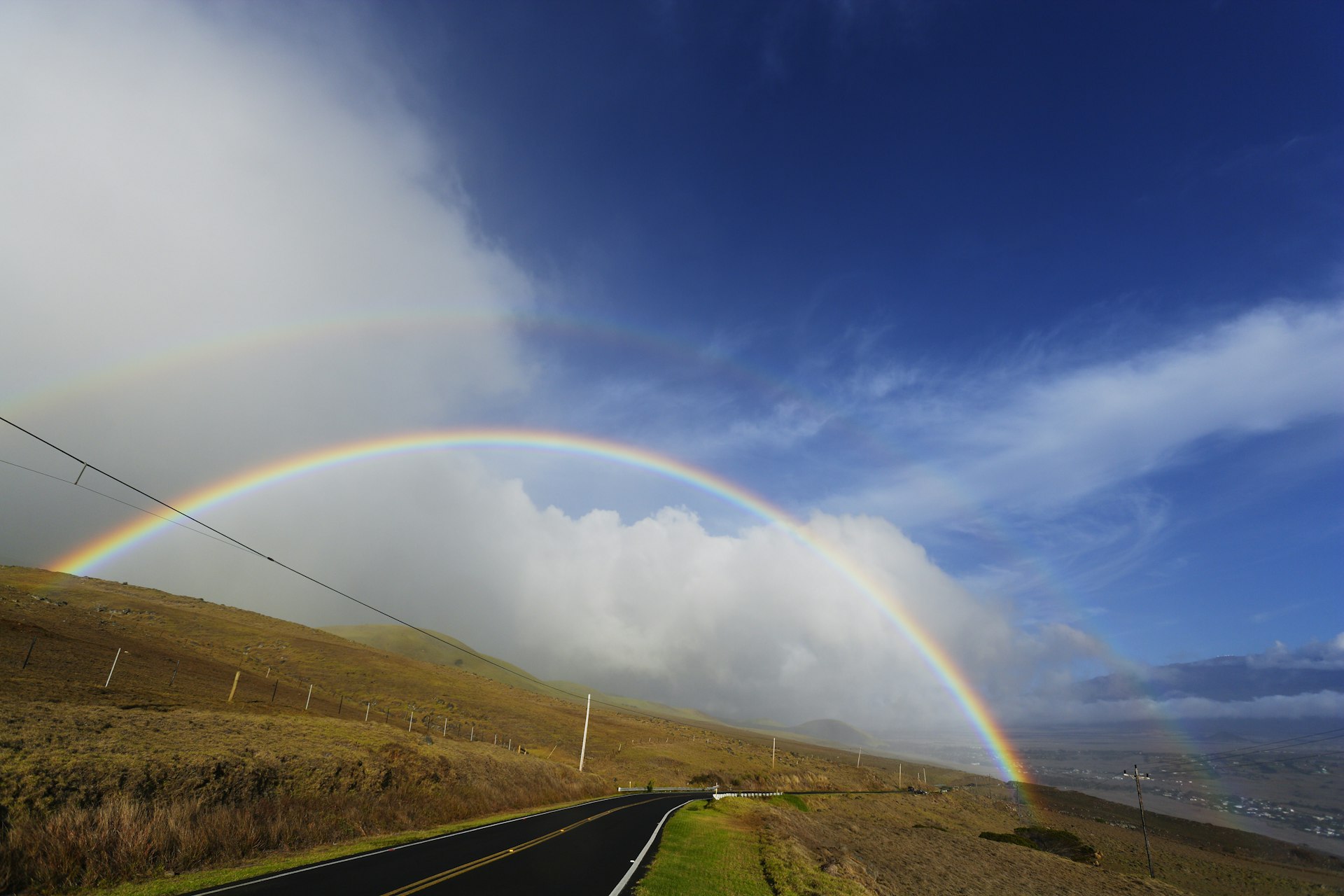 Rainbow appearing over the highway with Mauna Kea can be seen behind the rainbow