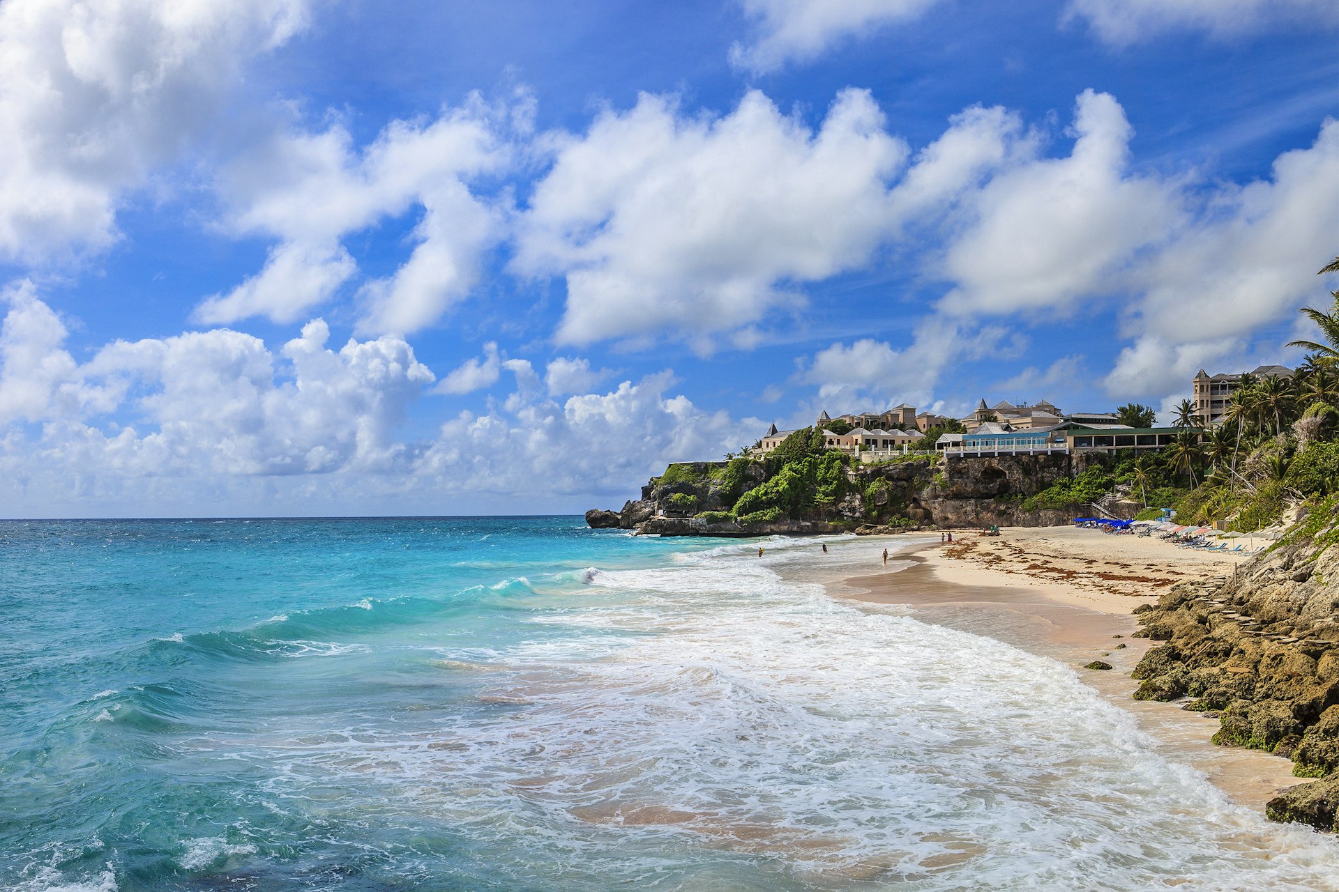 Aerial view of Crane Beach with white foam waves crashing on the sand. You can see a hotel on the high green cliffs.